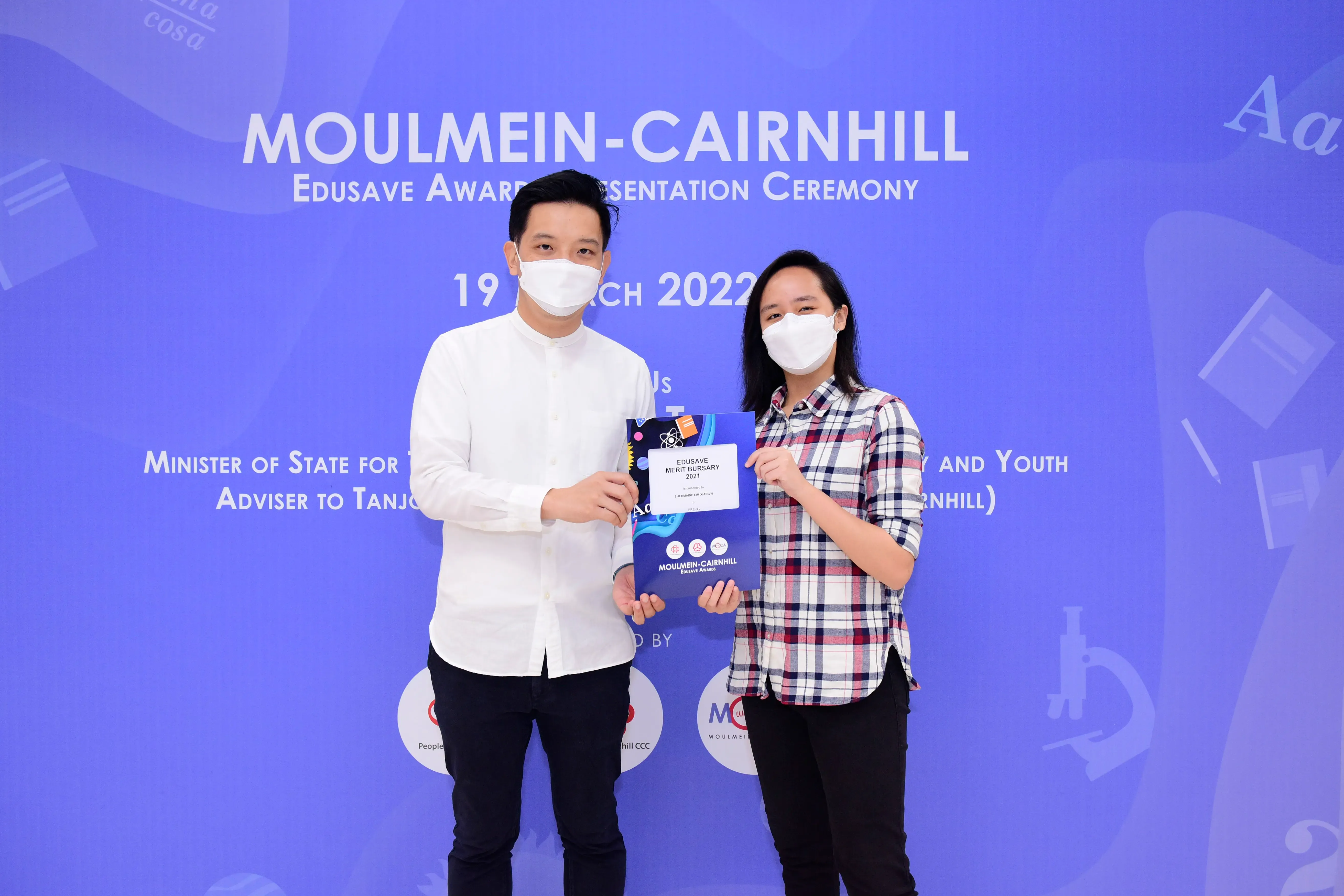 Two masked people hold an Edusave Merit Bursary certificate at the Moulmein-Cairnhill Edusave Award Ceremony 2022.