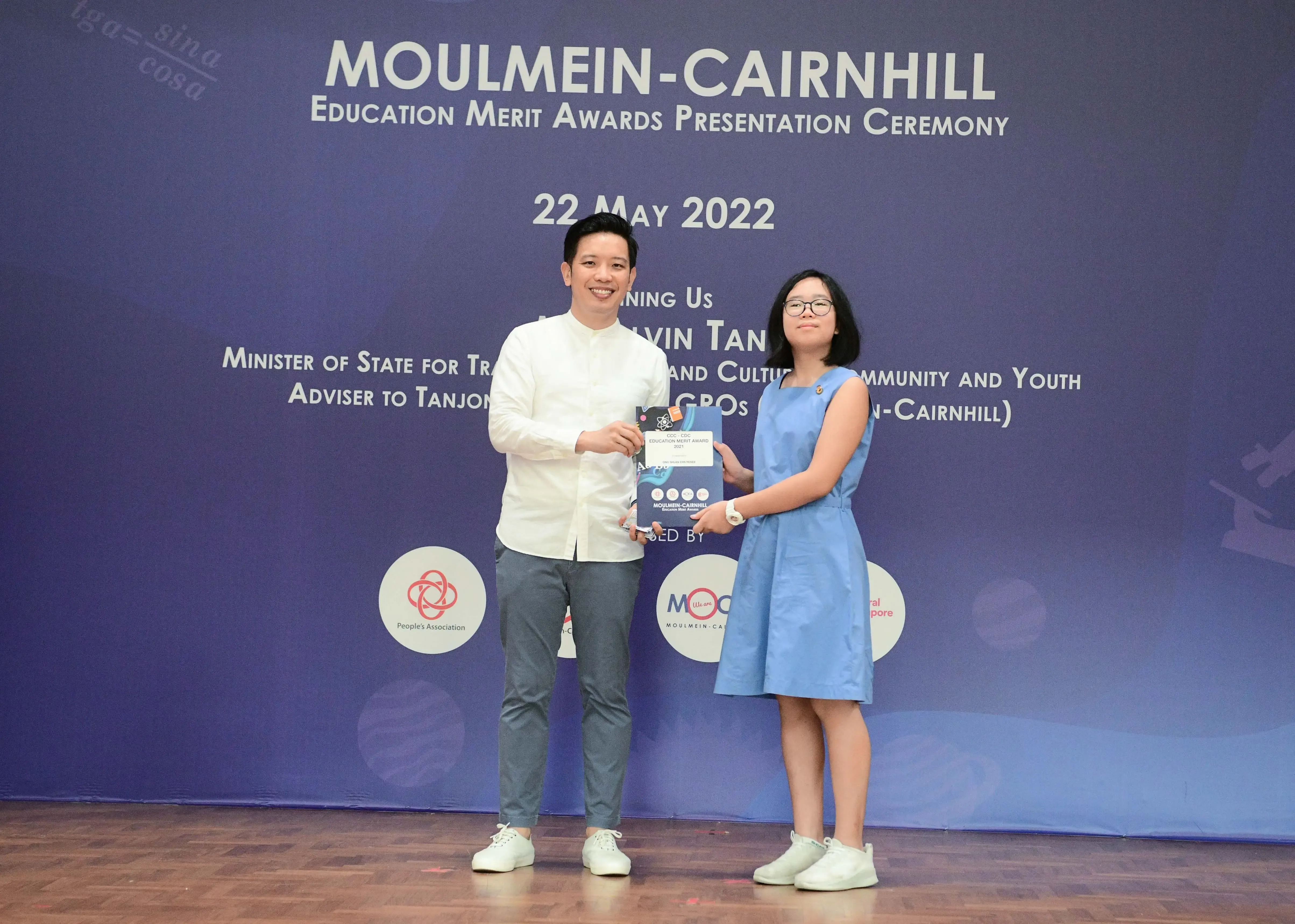 Two people hold an award certificate on stage at the Moulmein-Cairnhill Education Merit Awards on 22 May 2022.