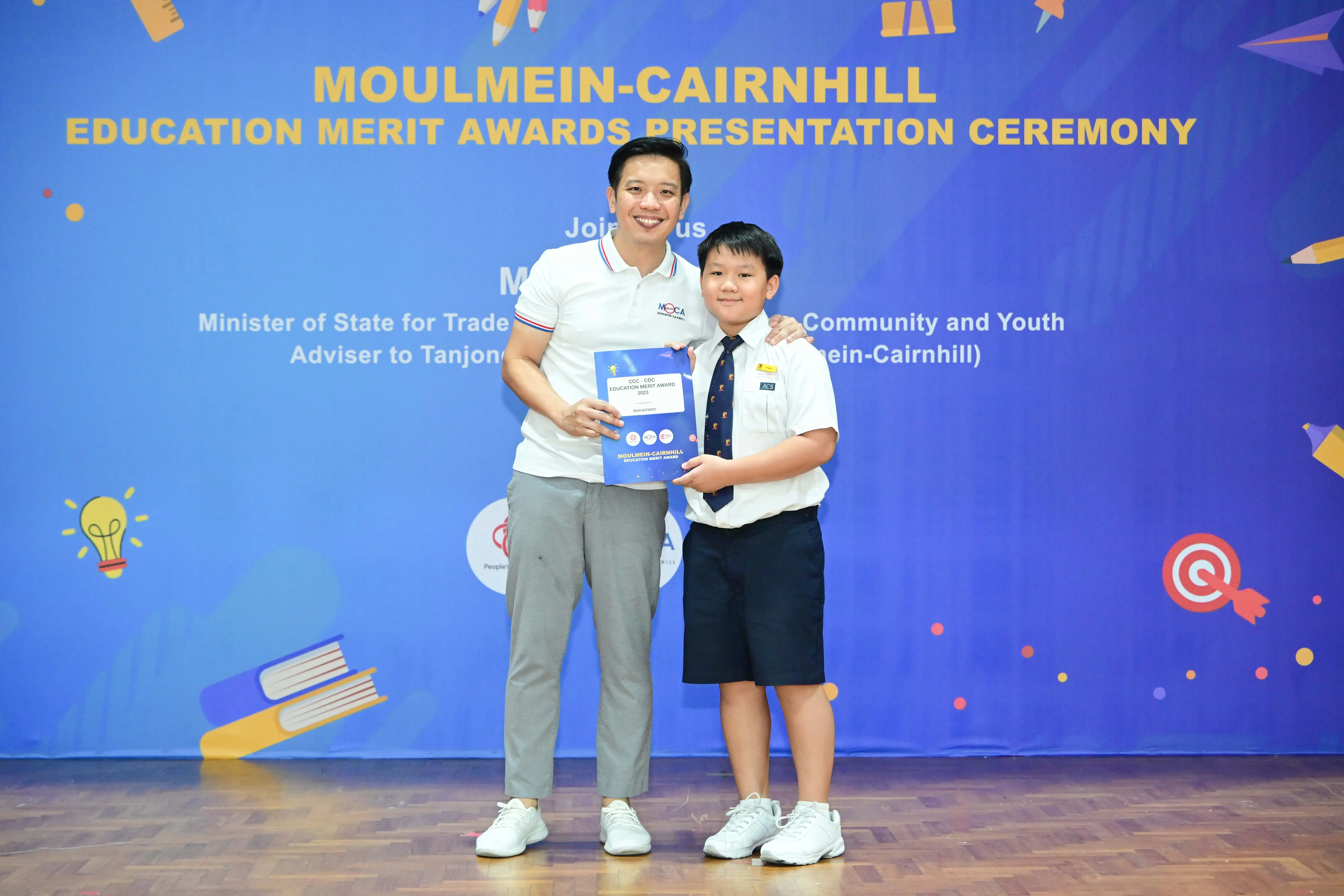 Man and young boy in school uniform hold an award certificate at Moulmein-Cairnhill Education Merit Awards ceremony.