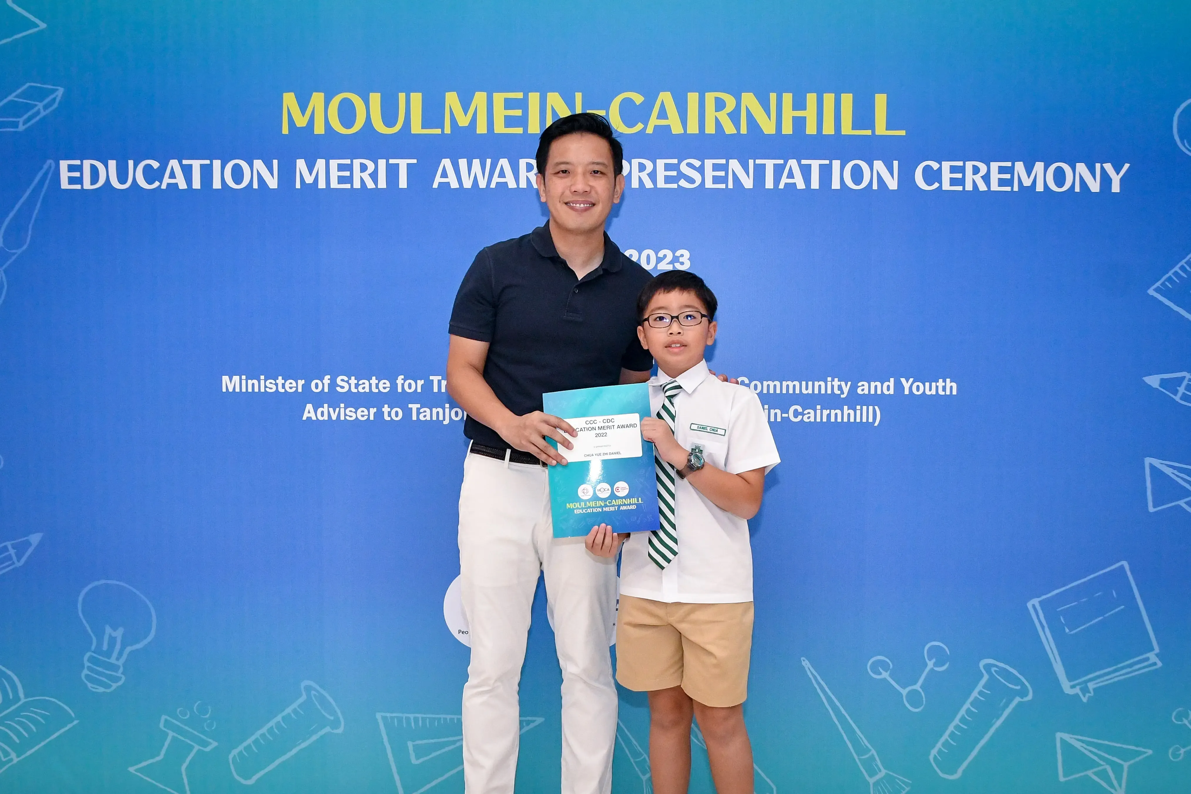 A man and a young boy hold an award certificate at the 2023 Moulmein-Cairnhill Education Merit Award Presentation Ceremony.