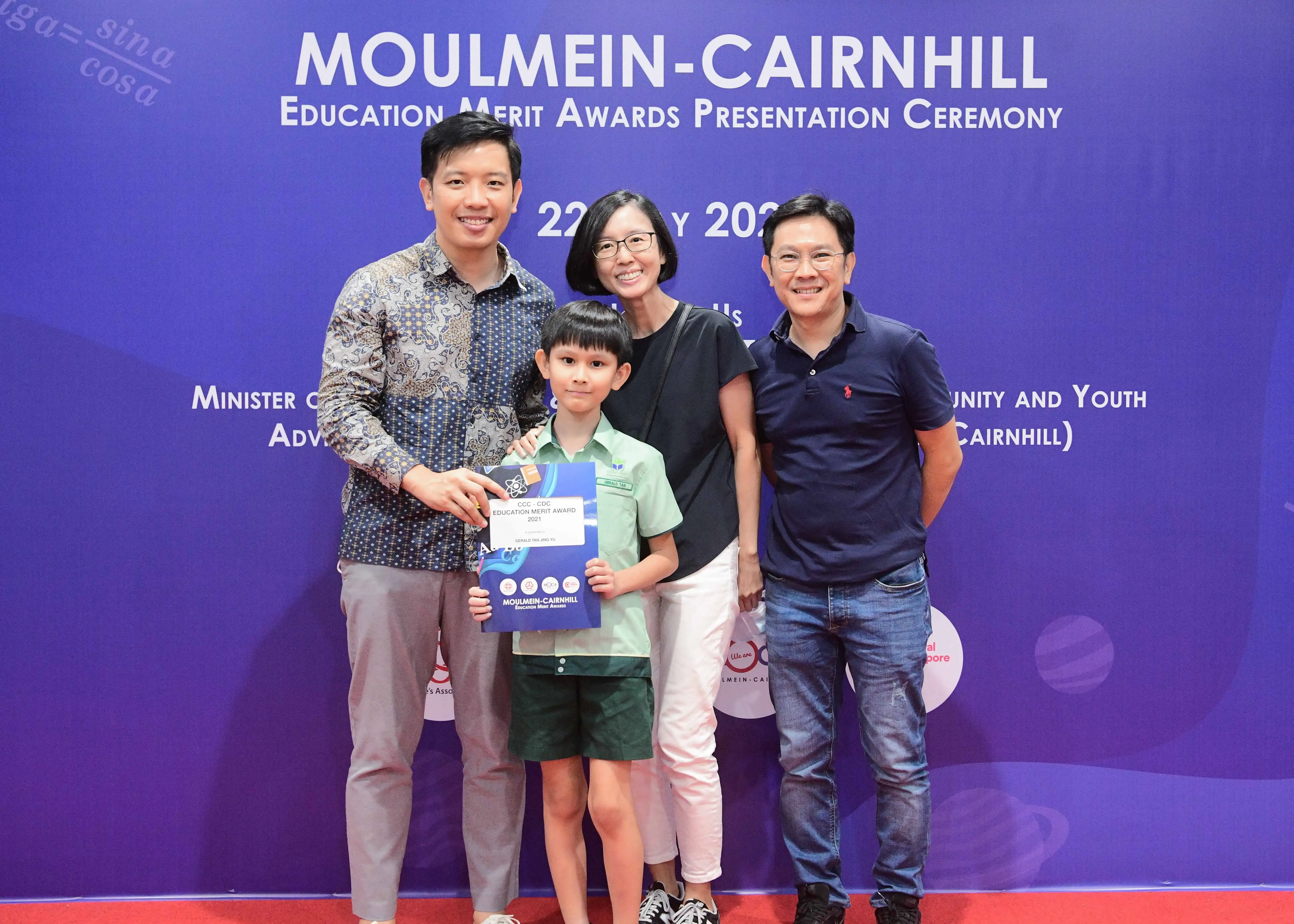 Four people pose at the Moulmein-Cairnhill Education Merit Awards ceremony, with a young boy holding an award certificate.