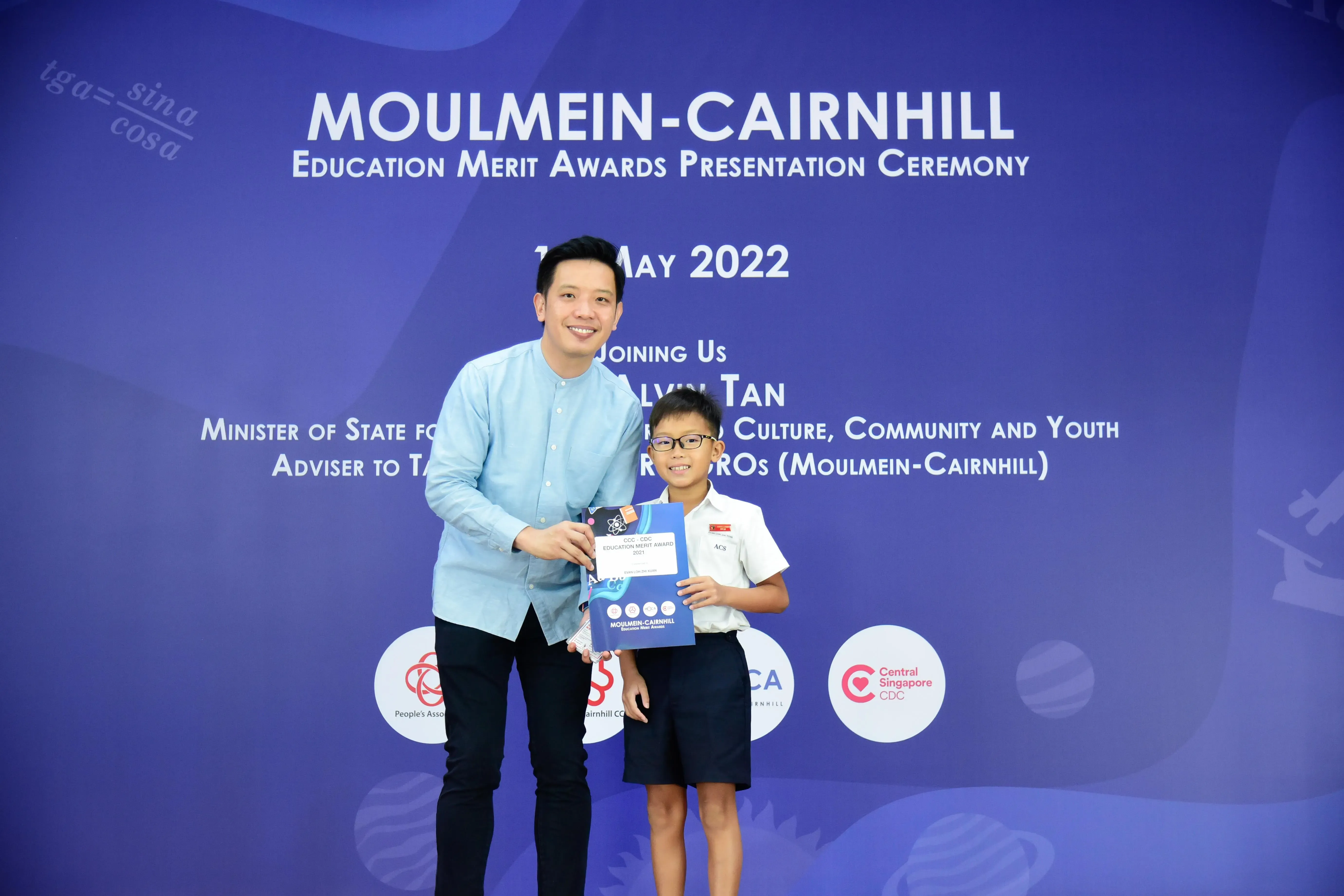 A man and a young boy holding an award certificate at the Moulmein-Cairnhill Education Merit Awards ceremony, May 2022.