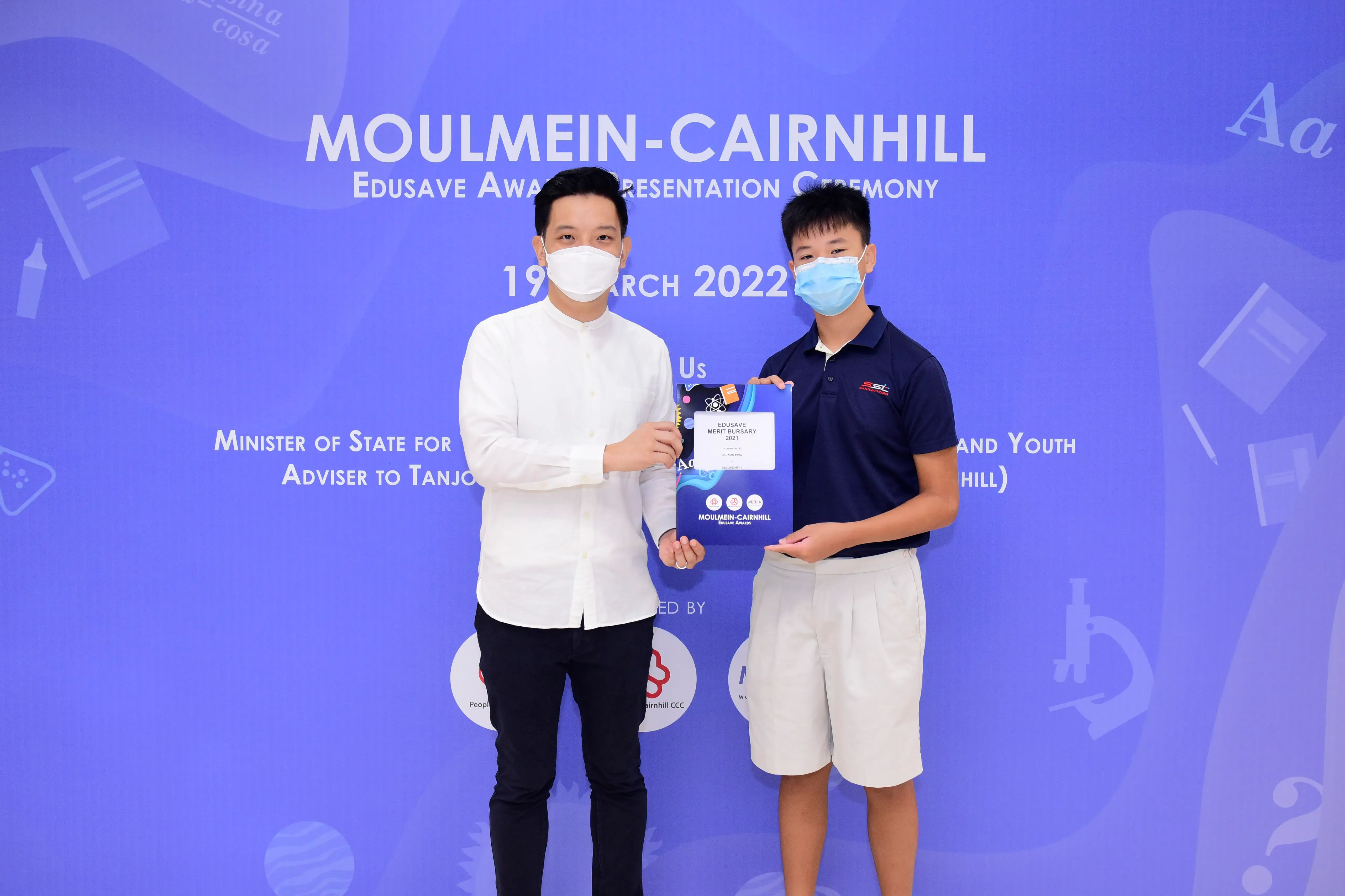 Two masked men hold a certificate at the Moulmein-Cairnhill Edusave Award Presentation Ceremony, March 2022.