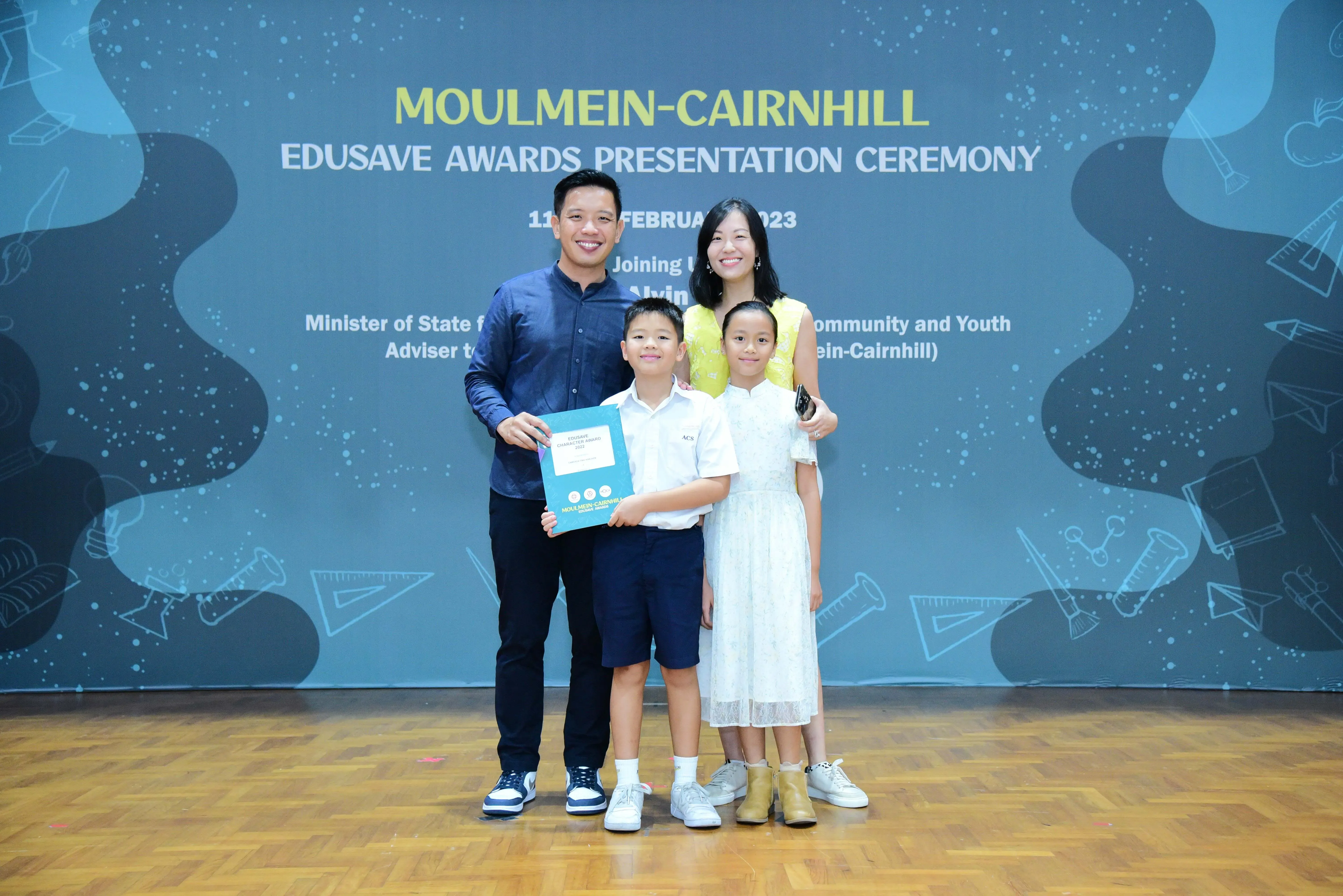 Family of four posing at the Moulmein-Cairnhill Edusave Awards Presentation Ceremony 2023 backdrop.