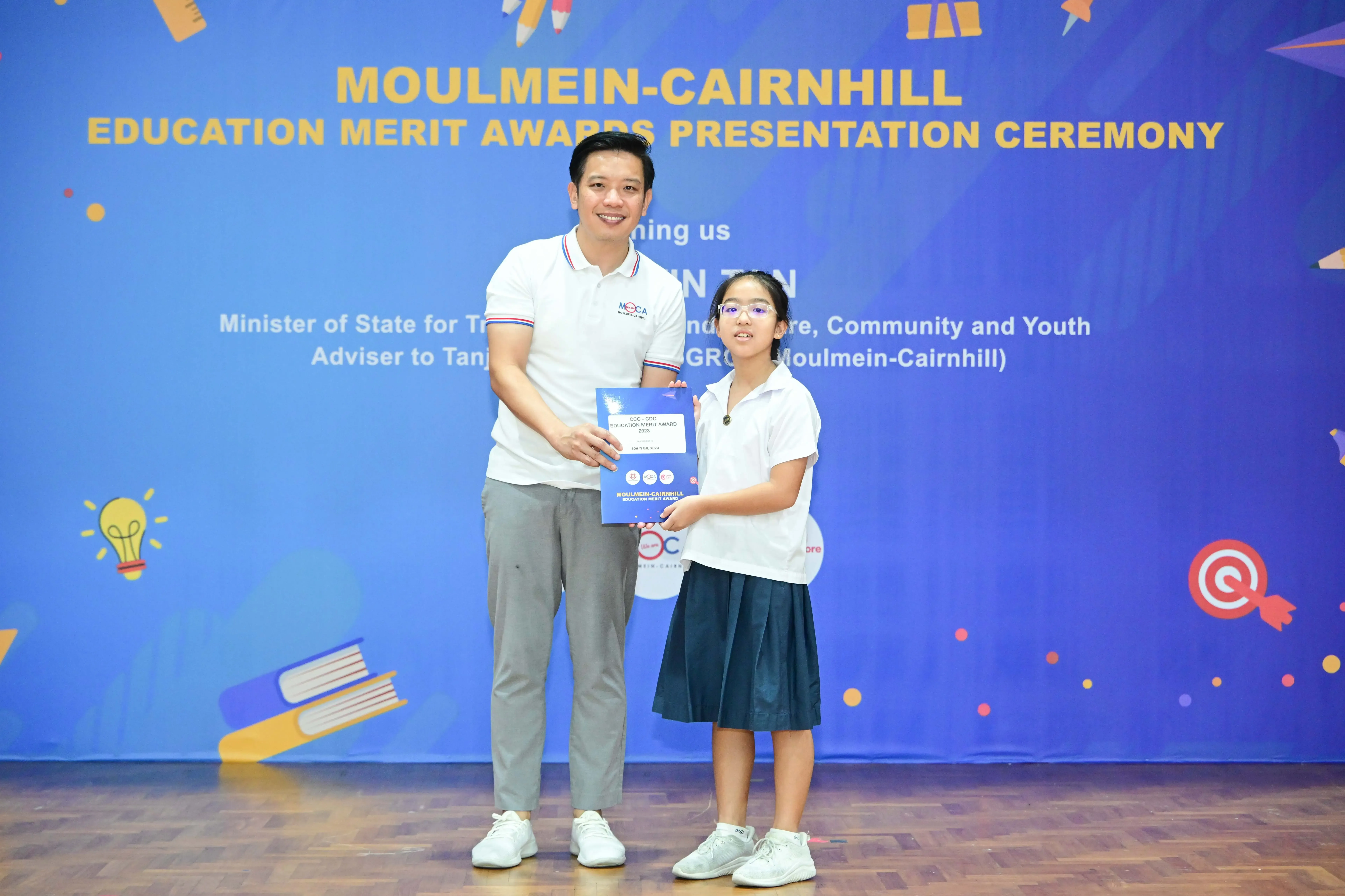 A man and a young girl hold a certificate together at the Moulmein-Cairnhill Education Merit Awards Presentation Ceremony.