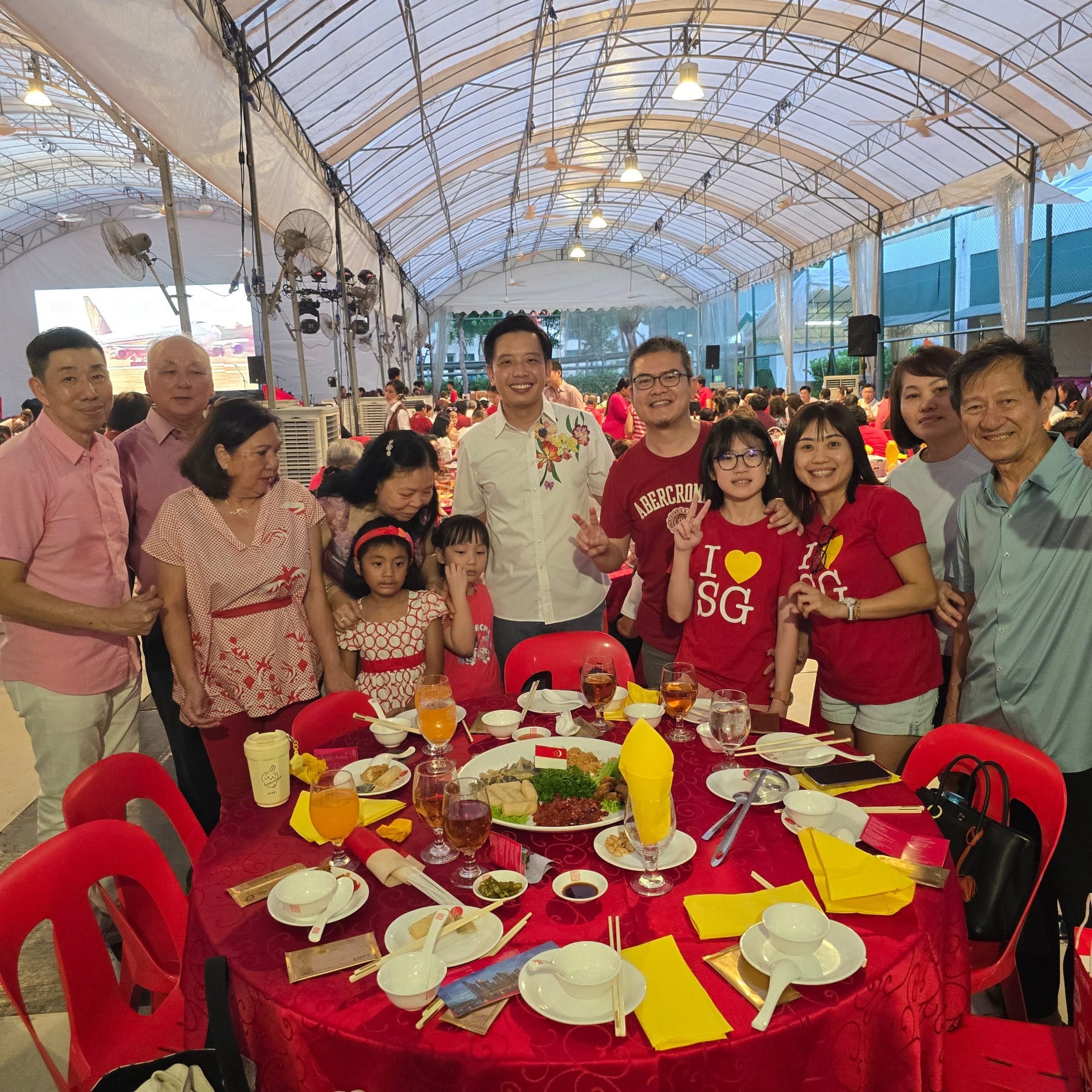 A group of people in red and pink outfits pose around a round banquet table at a festive outdoor event.