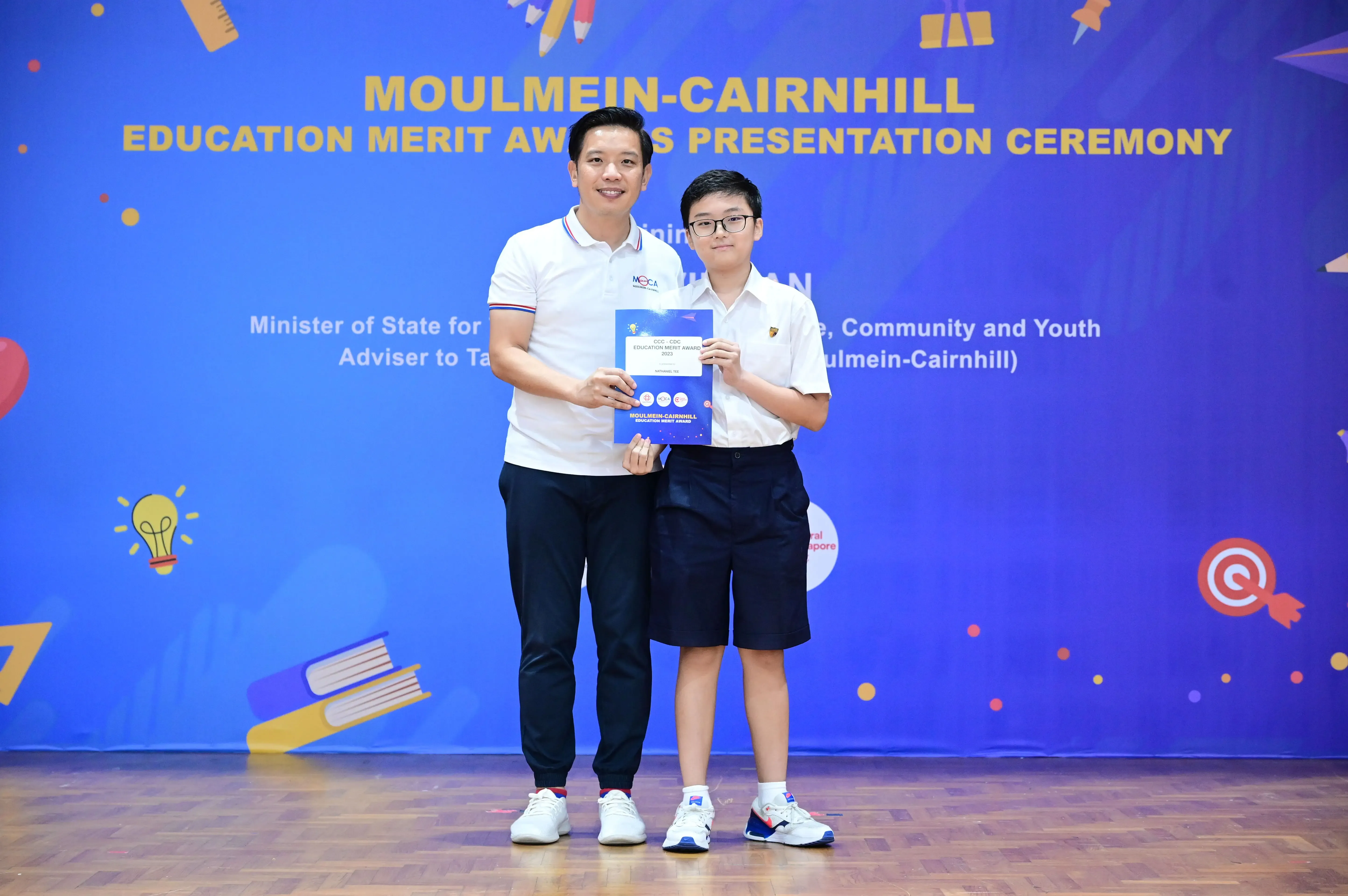 A man and a young student hold an award certificate at the Moulmein-Cairnhill Education Merit Awards ceremony.