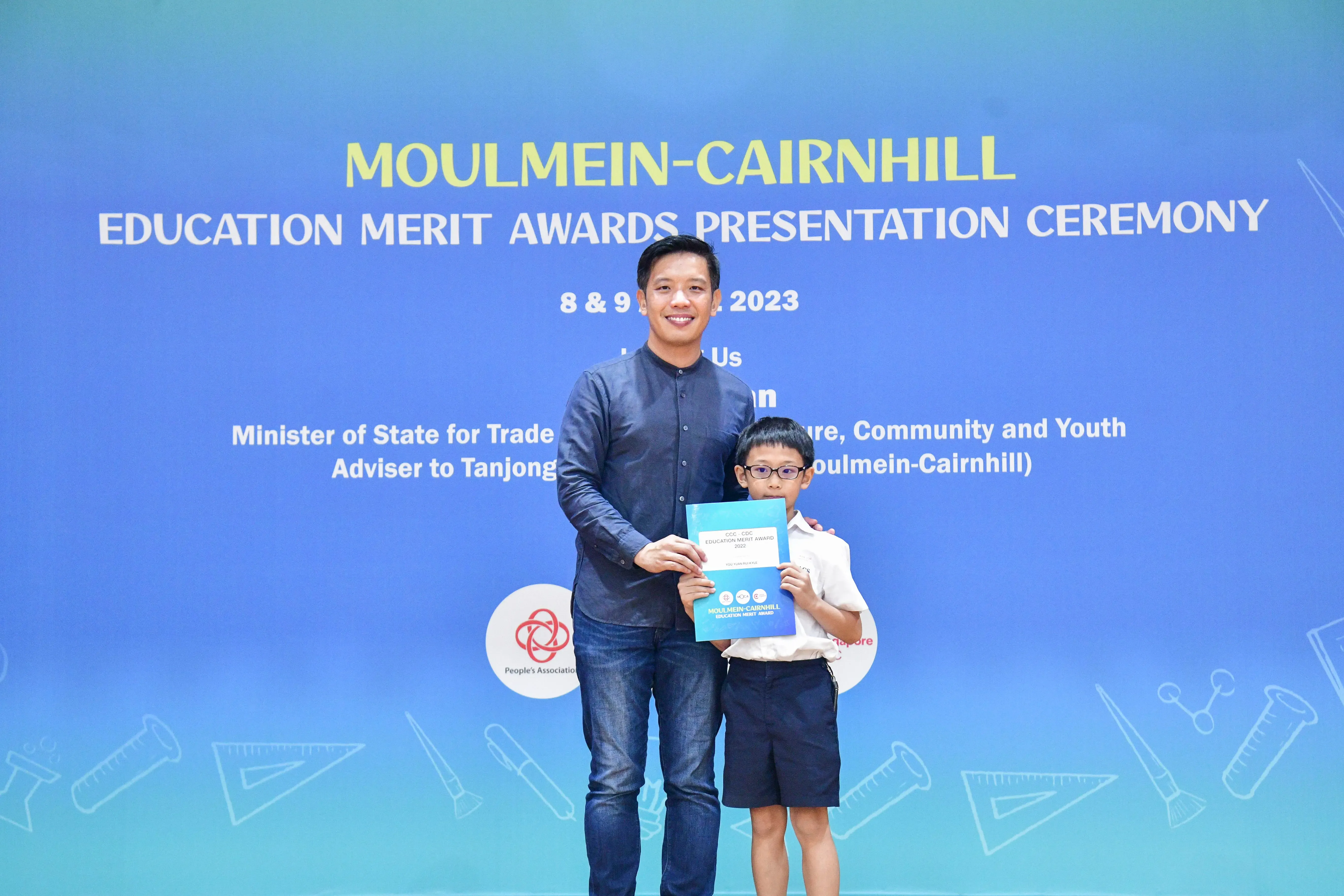 A man and a young boy hold a certificate together at the Moulmein-Cairnhill Education Merit Awards Ceremony 2023.
