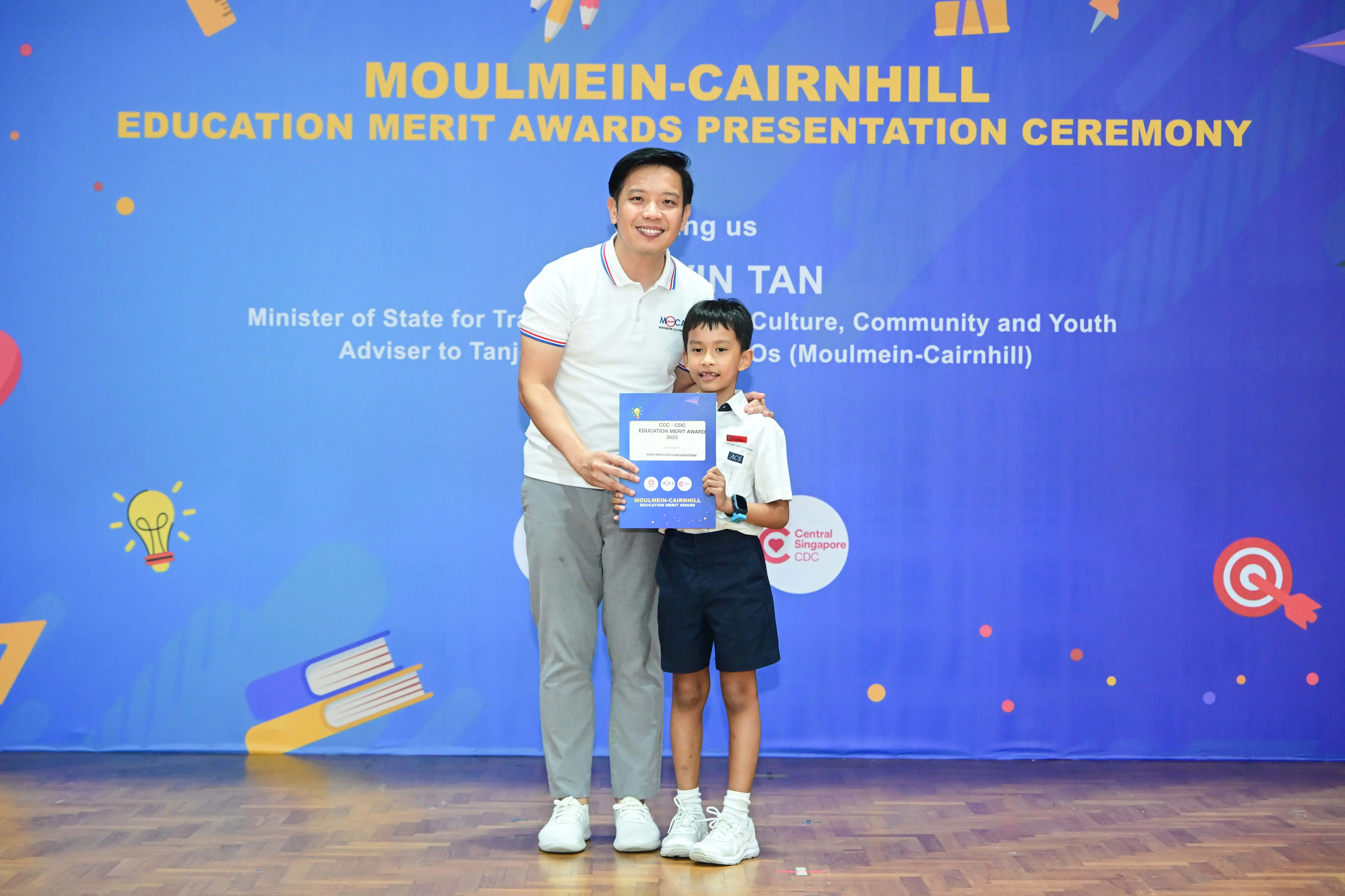 A man and a young boy hold a certificate at the Moulmein-Cairnhill Education Merit Awards Presentation Ceremony.