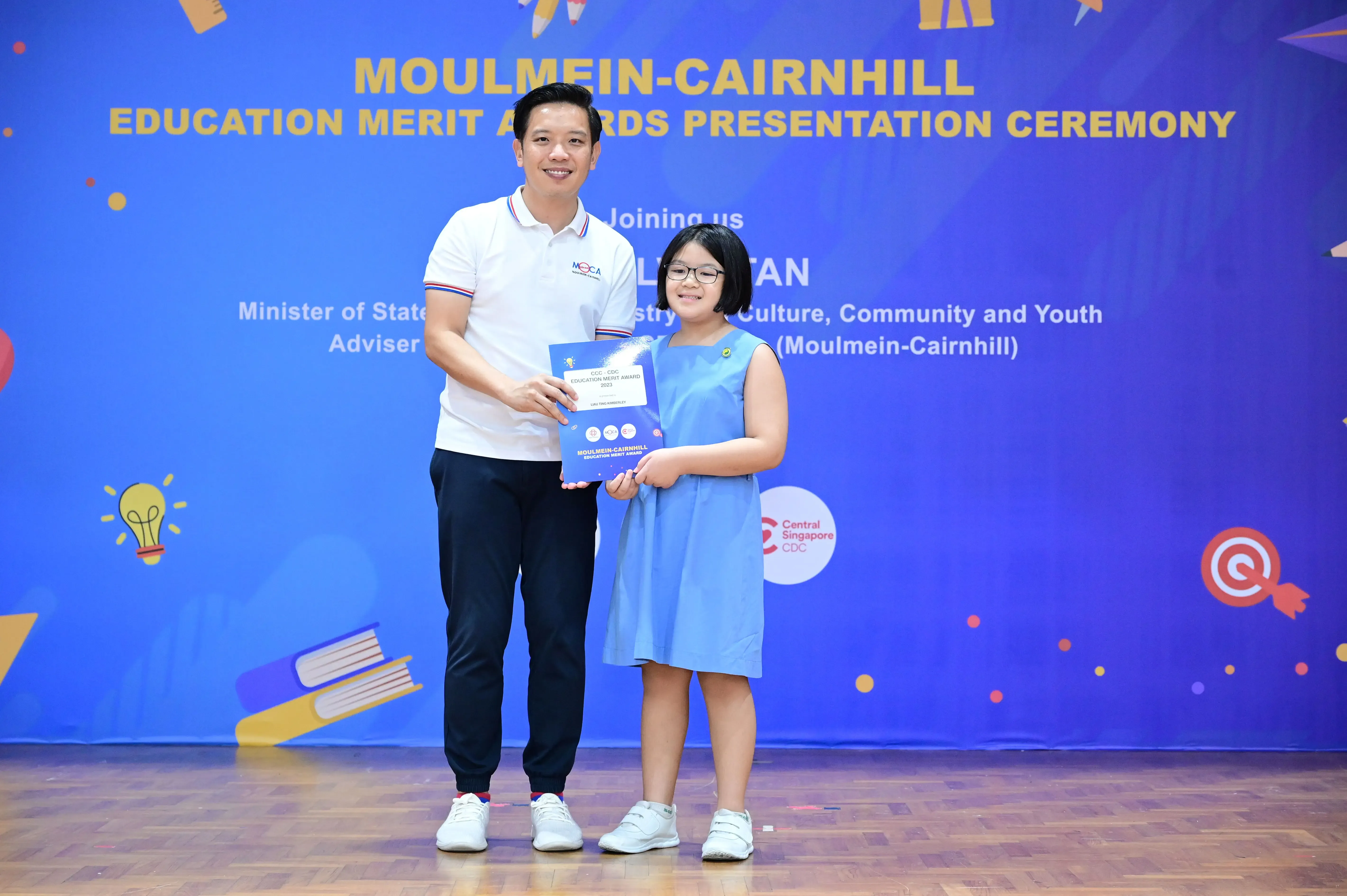 A man and a young girl hold a certificate at the Moulmein-Cairnhill Education Merit Awards Presentation Ceremony.
