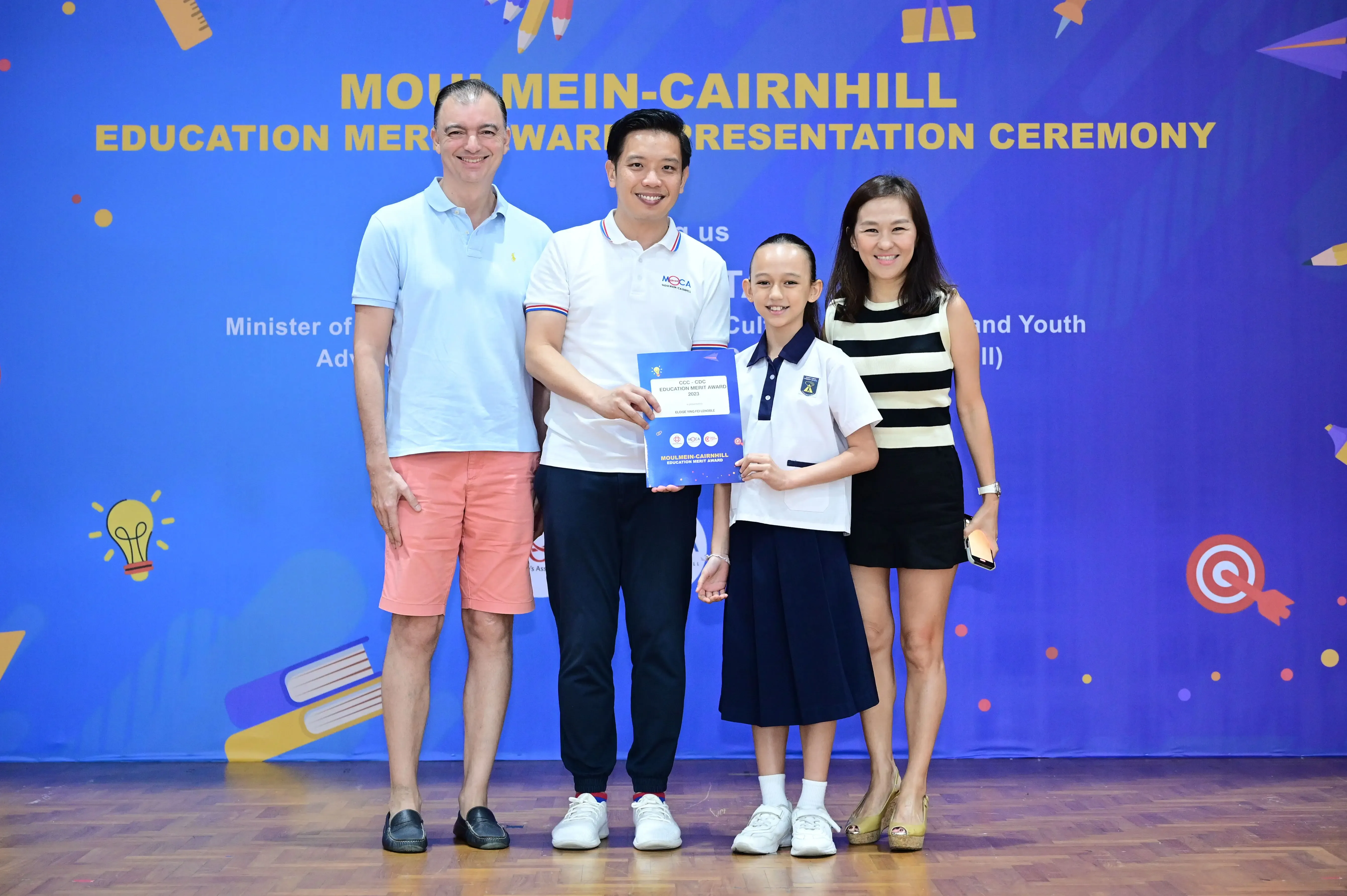 Four people pose at the Moulmein-Cairnhill Education Merit Award Presentation Ceremony, with a child holding an award certificate.