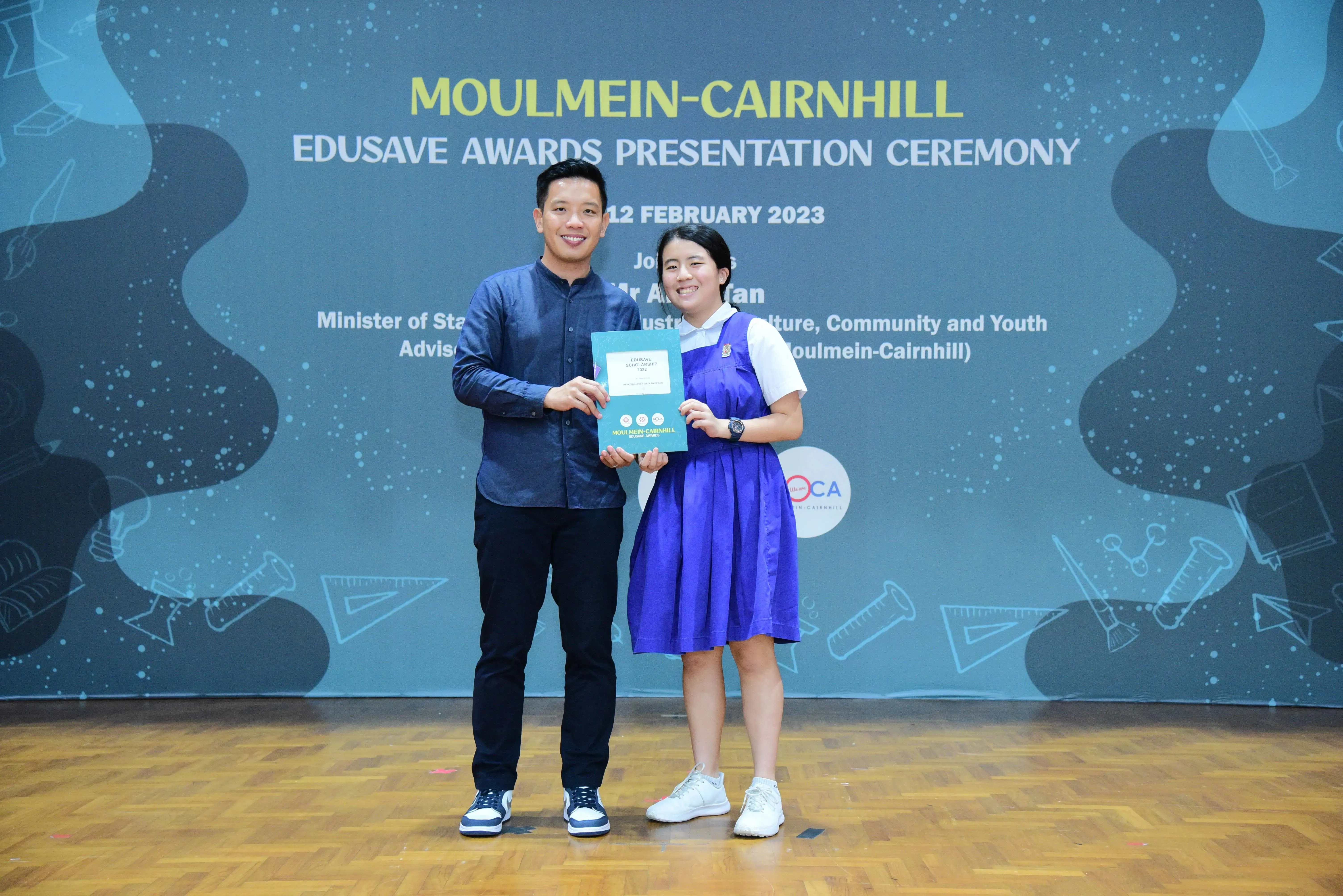 Two people smile holding a certificate at the Moulmein-Cairnhill Edusave Awards Presentation Ceremony, February 2023.