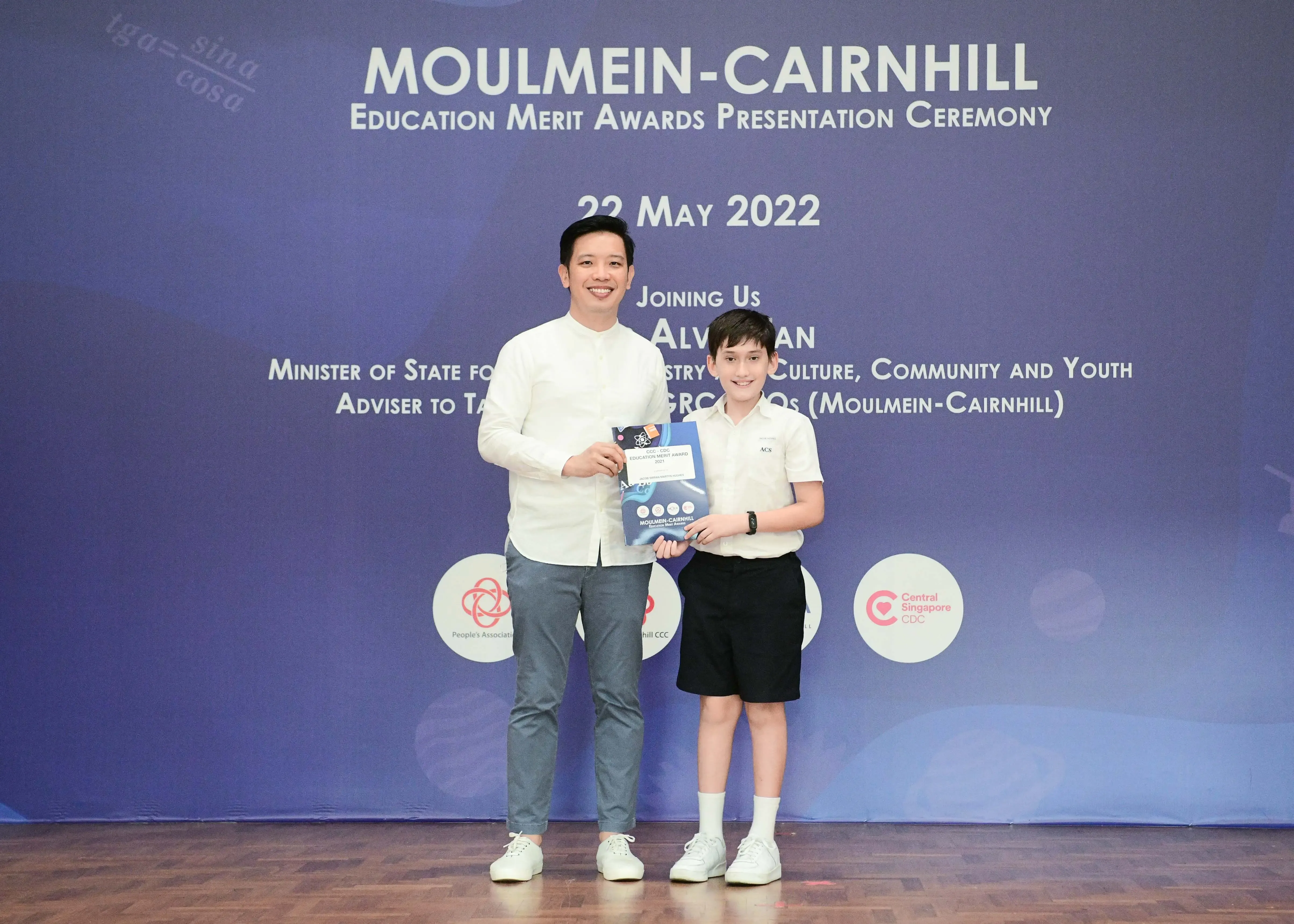 An adult and a young boy hold an award booklet at the Moulmein-Cairnhill Education Merit Awards ceremony on 22 May 2022.