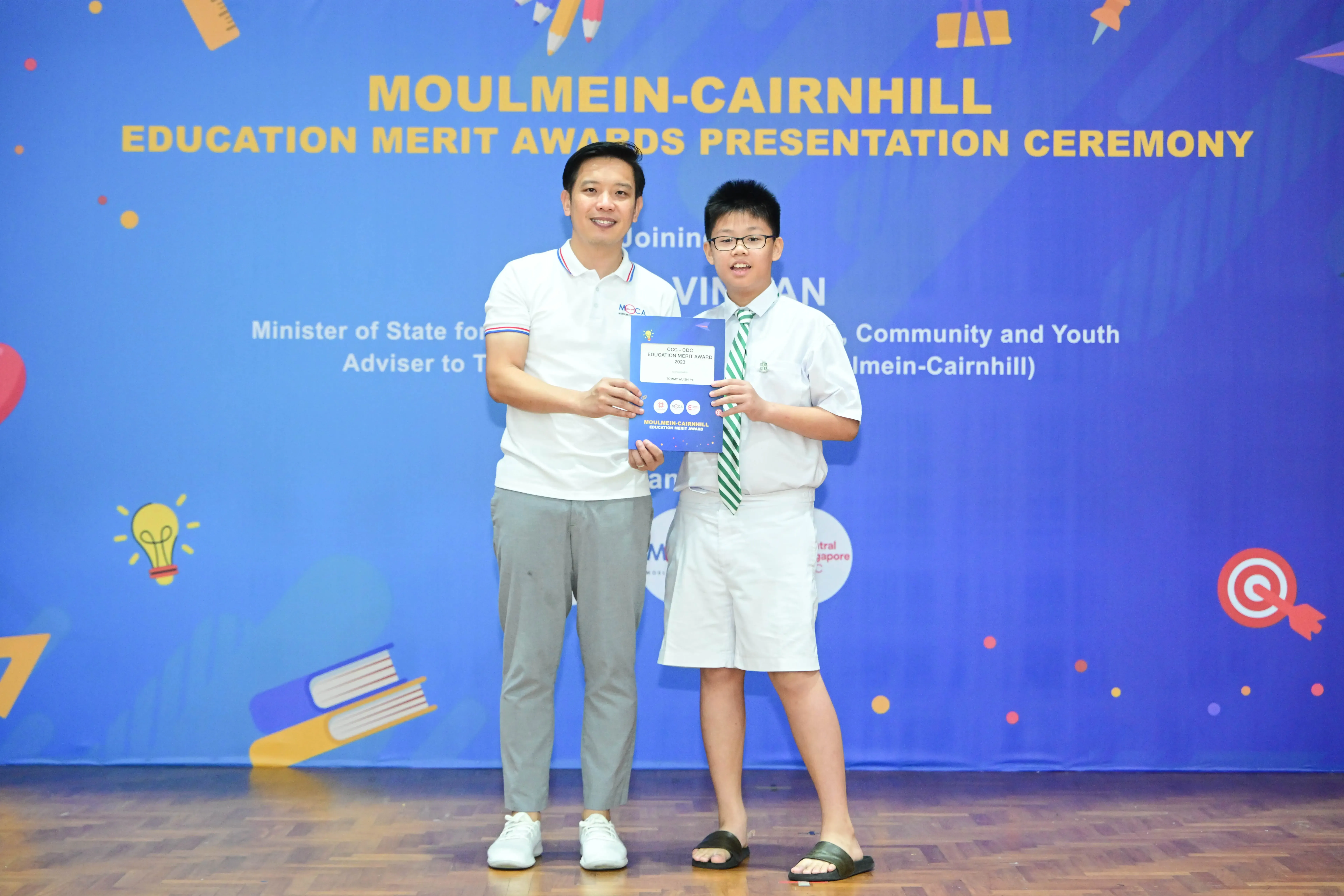 A man and a boy hold an award certificate at the Moulmein-Cairnhill Education Merit Awards Presentation Ceremony.