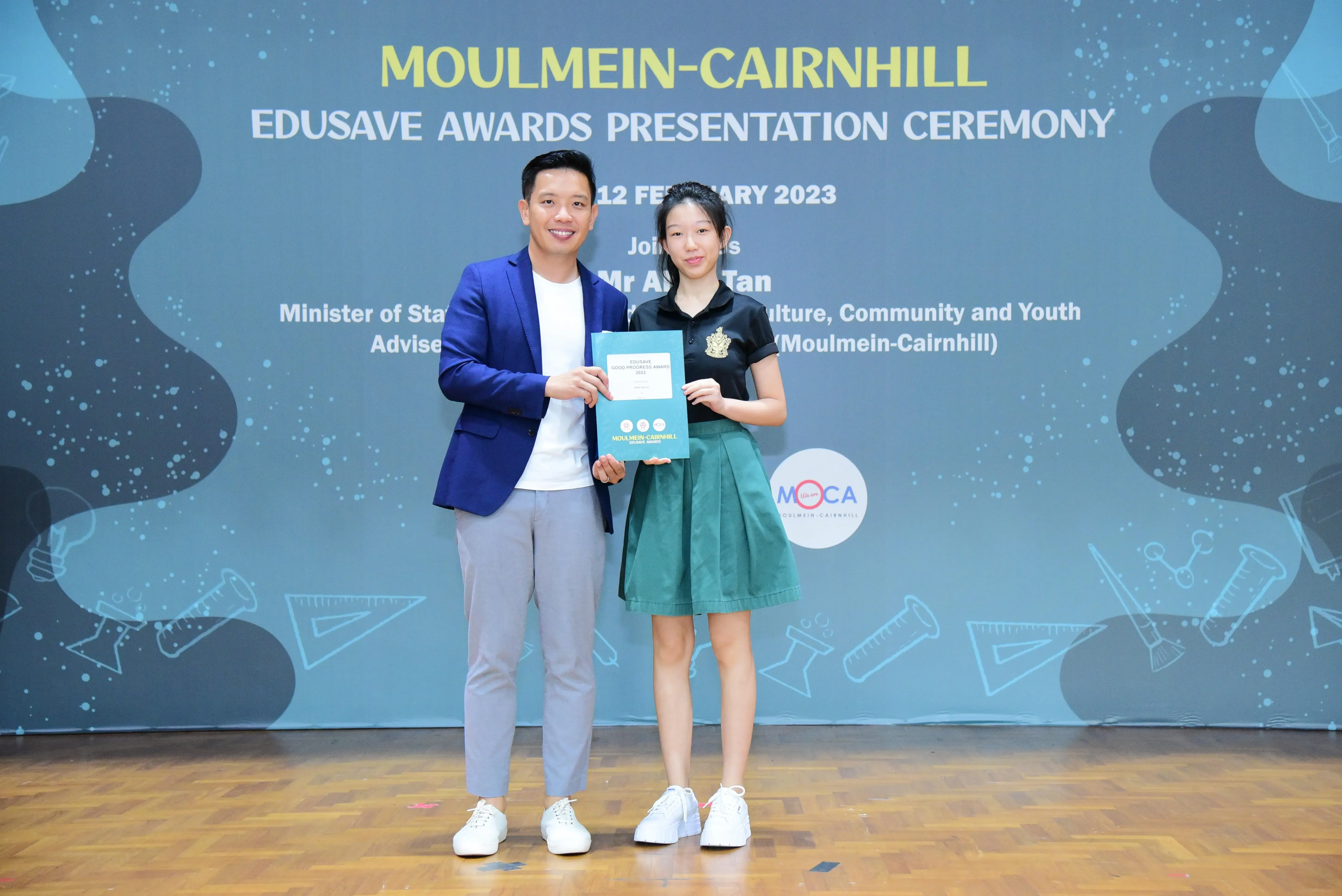 A man in a blue blazer and a girl in school uniform hold an award at the Moulmein-Cairnhill Edusave Awards Ceremony.