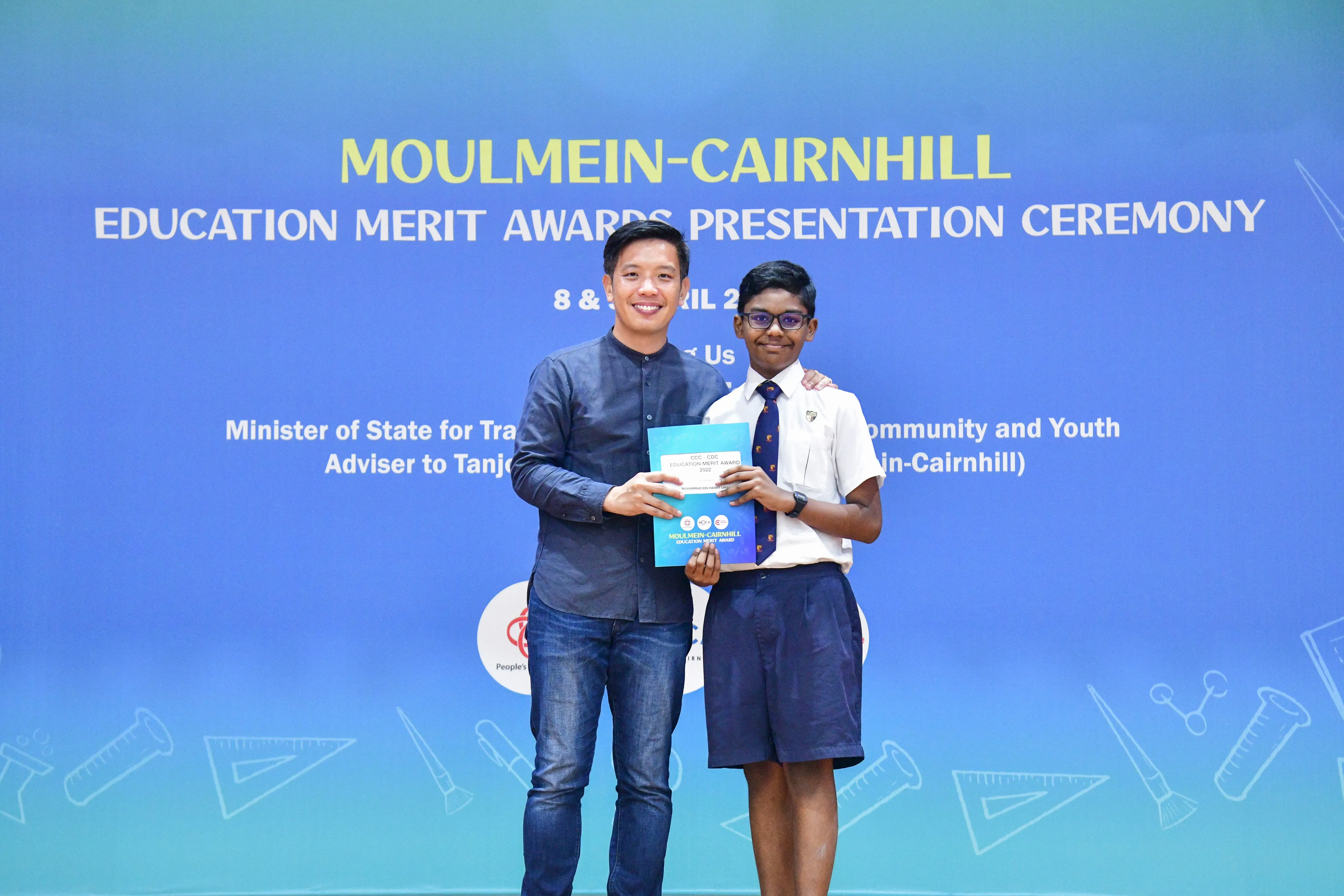 An adult and a uniformed student hold an award booklet at the Moulmein-Cairnhill Education Merit Awards Ceremony.
