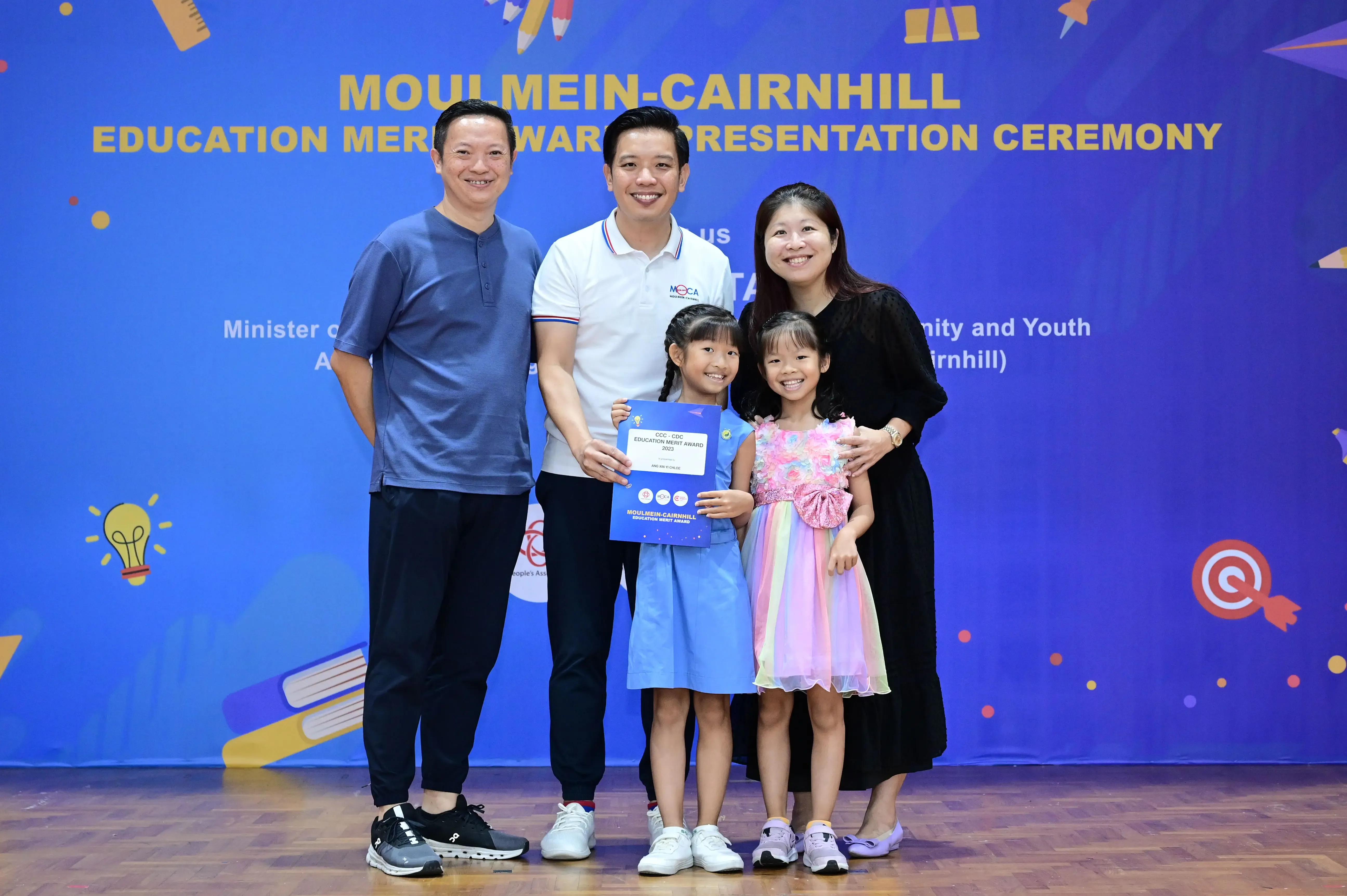 Two adults and two young girls pose with an award certificate at the Moulmein-Cairnhill Education Merit Award Presentation Ceremony.