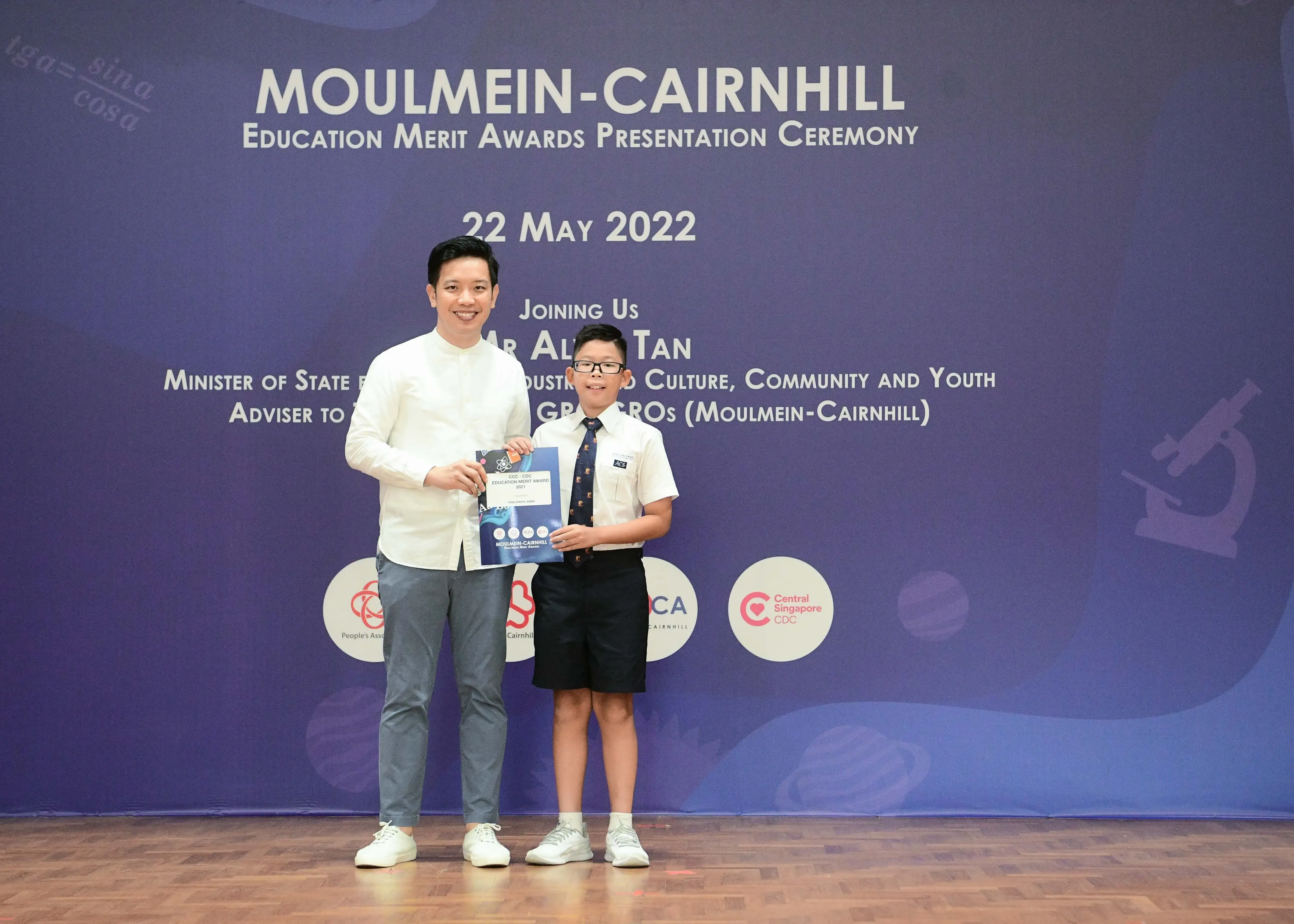 A man and a young boy hold a certificate at the Moulmein-Cairnhill Education Merit Awards Ceremony on 22 May 2022.