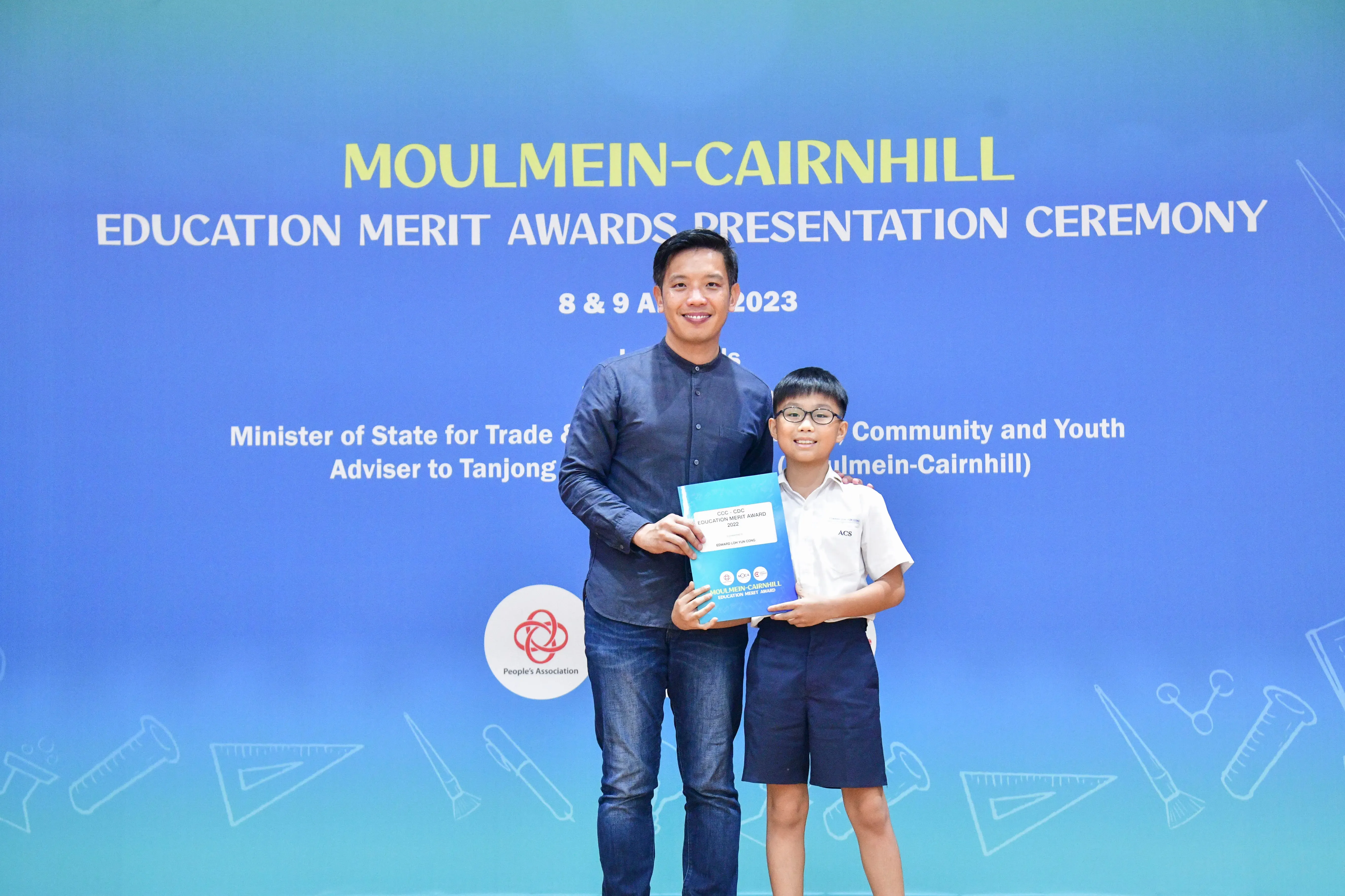 An adult and a young boy holding an award booklet at the Moulmein-Cairnhill Education Merit Awards Ceremony 2023.