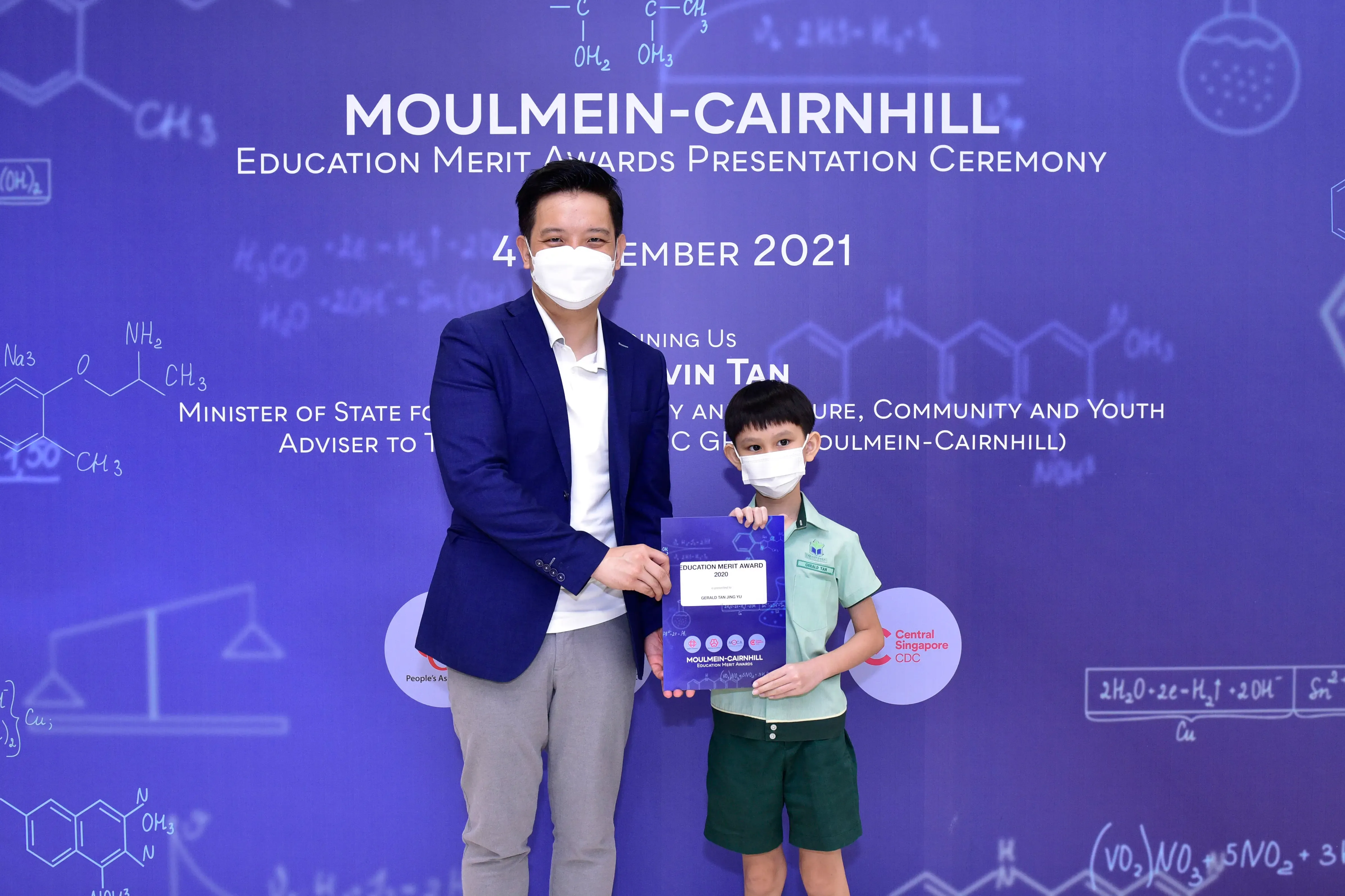 A masked man and young boy hold an award at the Moulmein-Cairnhill Education Merit Awards Ceremony 2021.