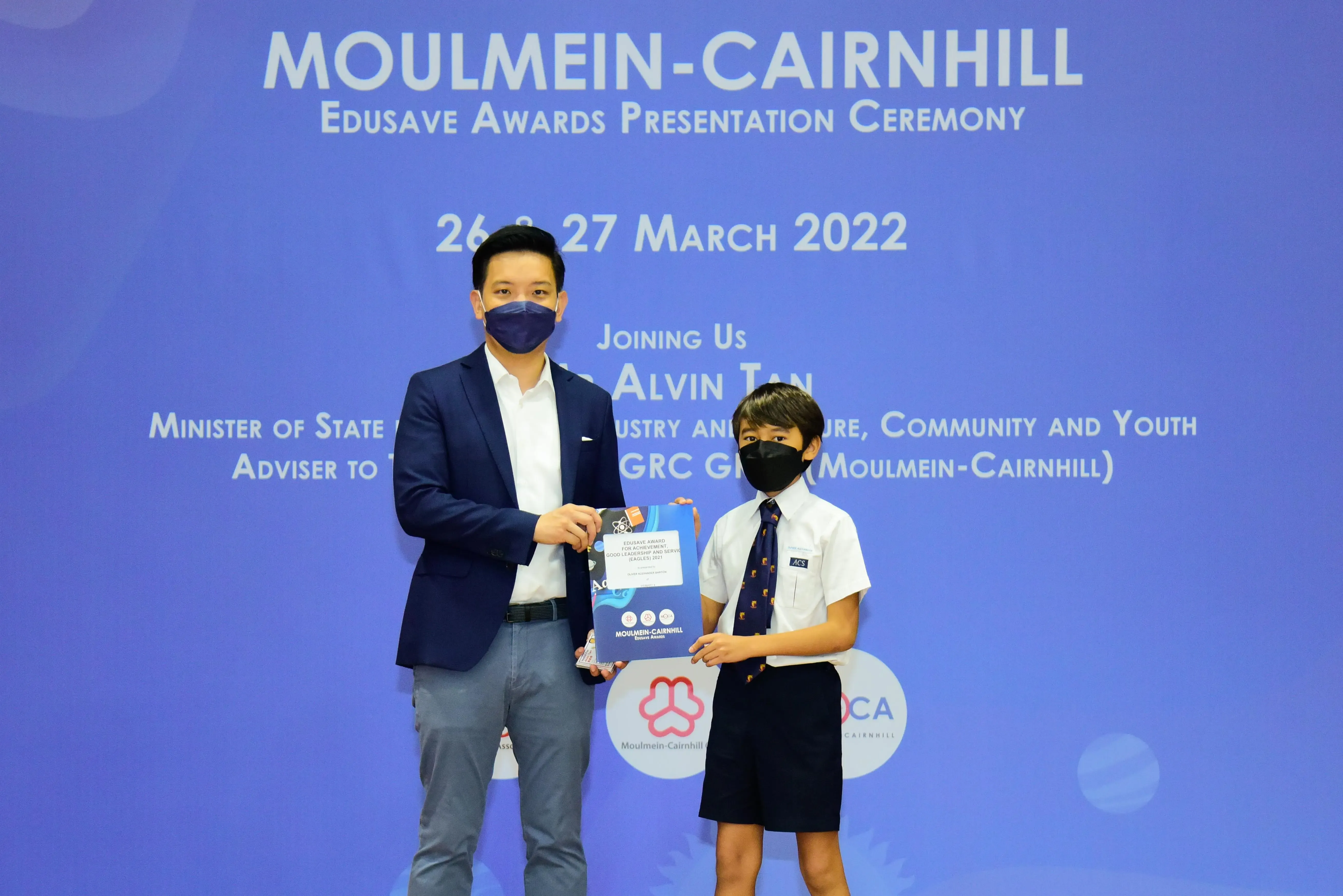 An adult and a masked student hold an award booklet at the Moulmein-Cairnhill Edusave Awards Ceremony, March 2022.