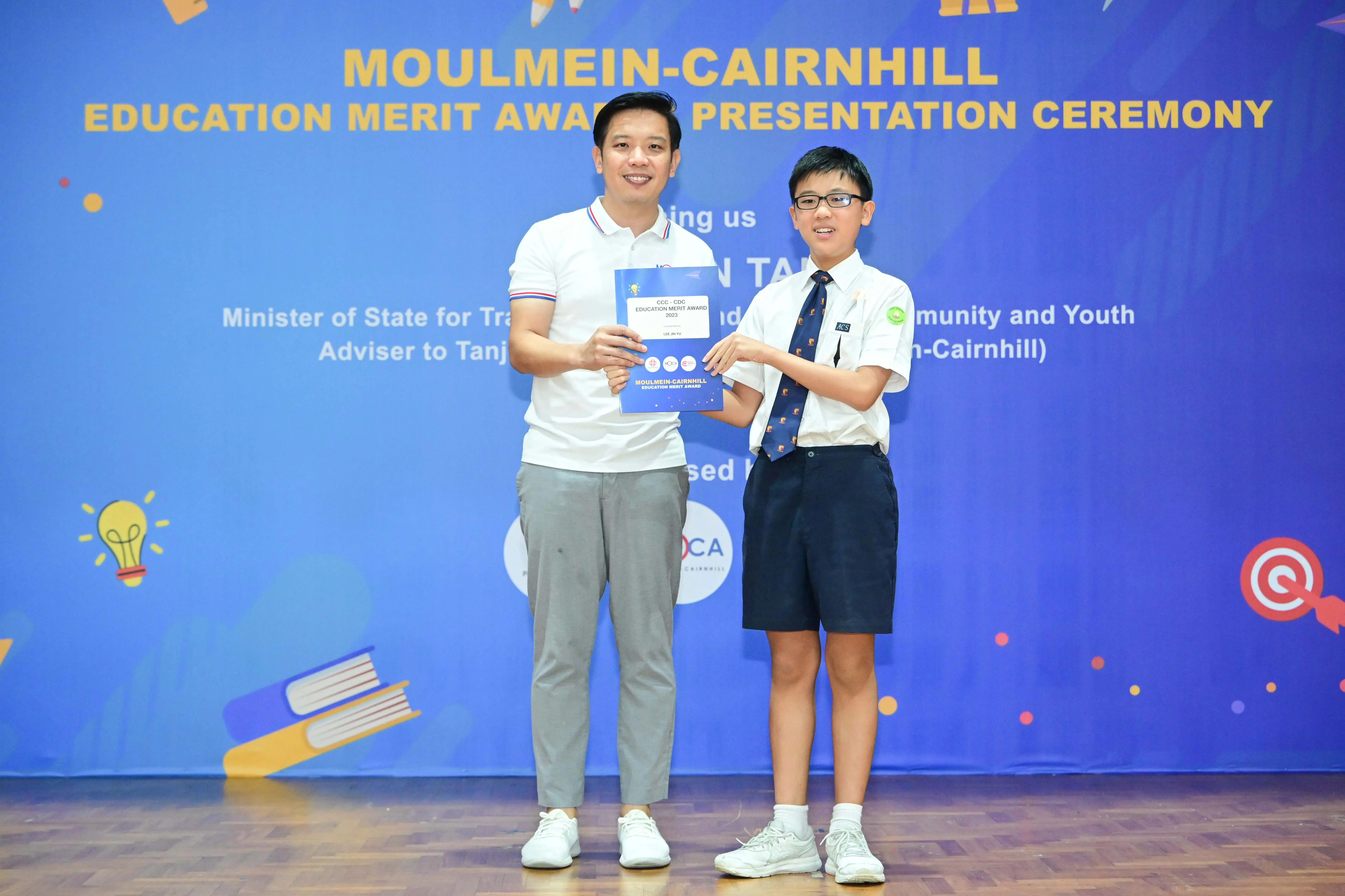 Two people hold a certificate together at the Moulmein-Cairnhill Education Merit Award Presentation Ceremony.