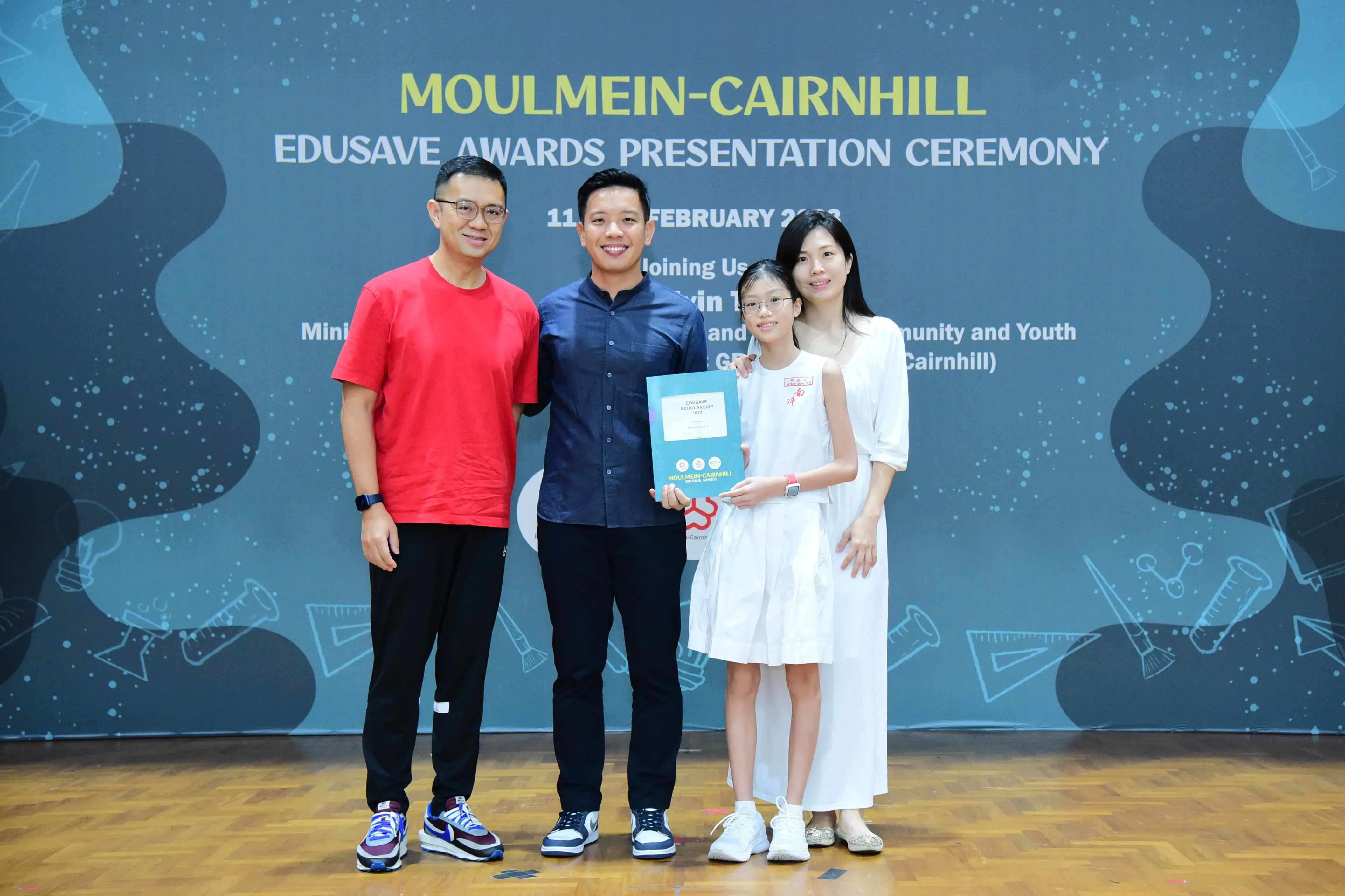 Four people pose with an award certificate at the Moulmein-Cairnhill Edusave Awards Presentation Ceremony backdrop.