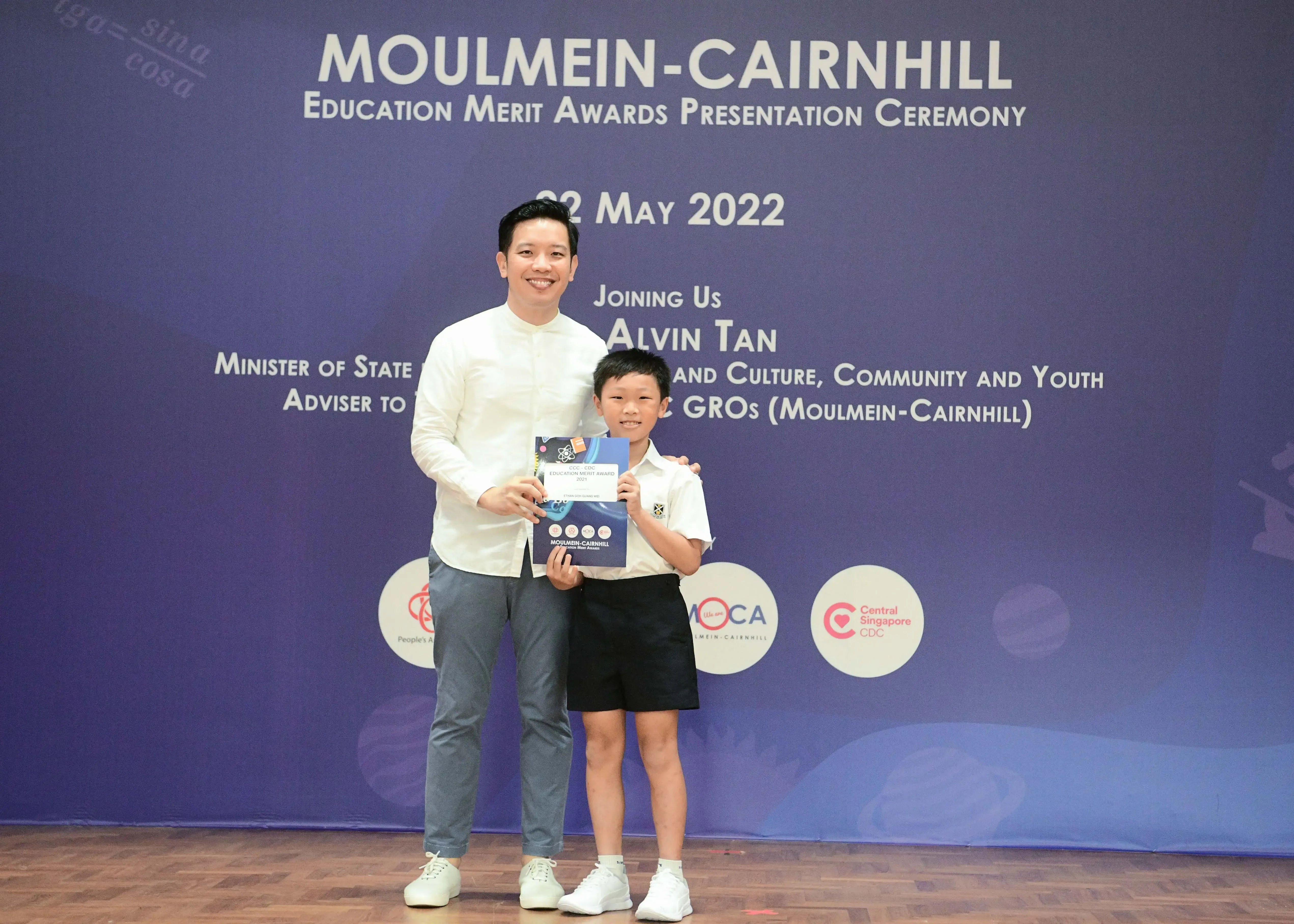 A man and a young boy pose holding an award certificate at the Moulmein-Cairnhill Education Merit Awards ceremony, May 2022.