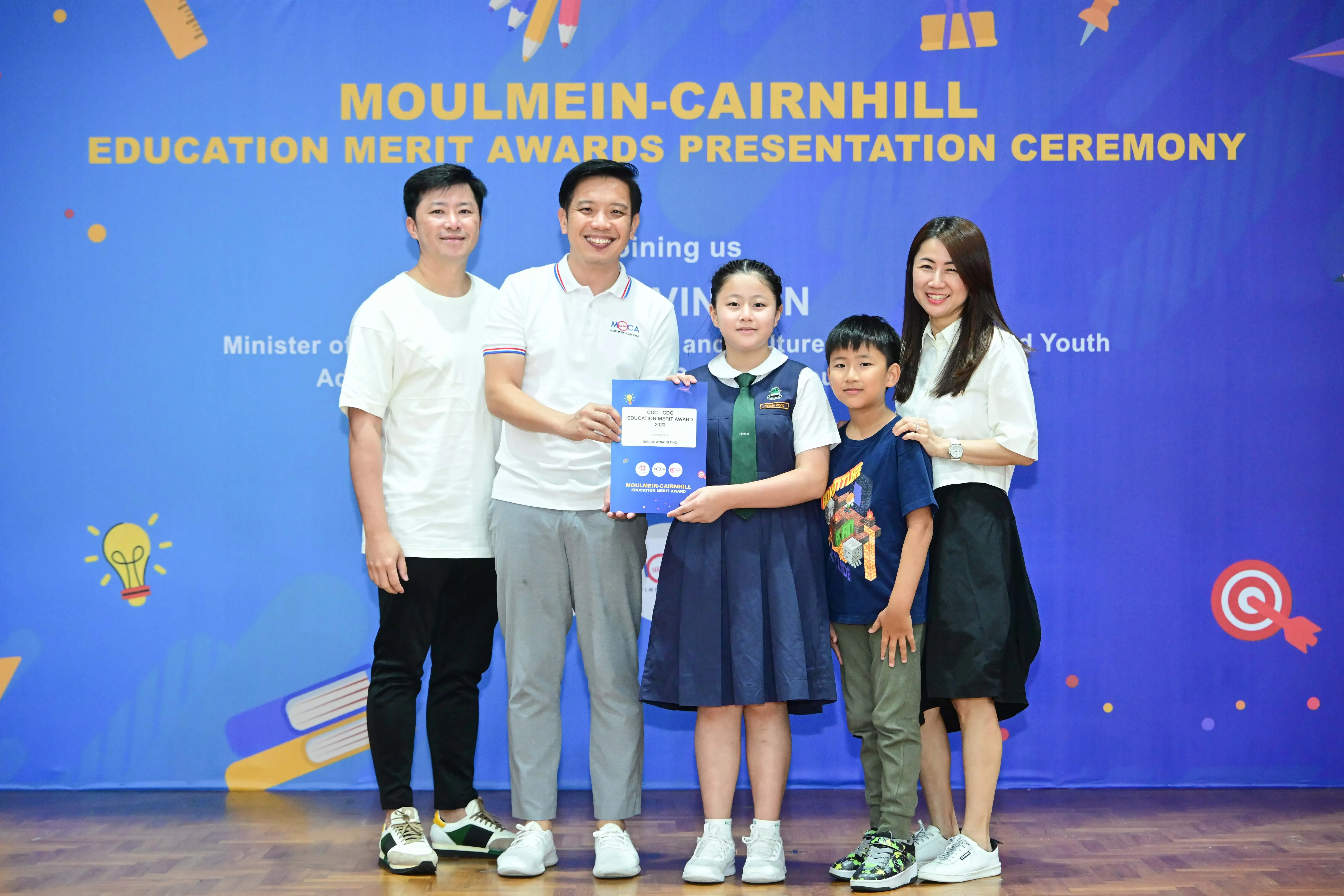 Two adults and two children pose with a certificate at the Moulmein-Cairnhill Education Merit Awards Ceremony.