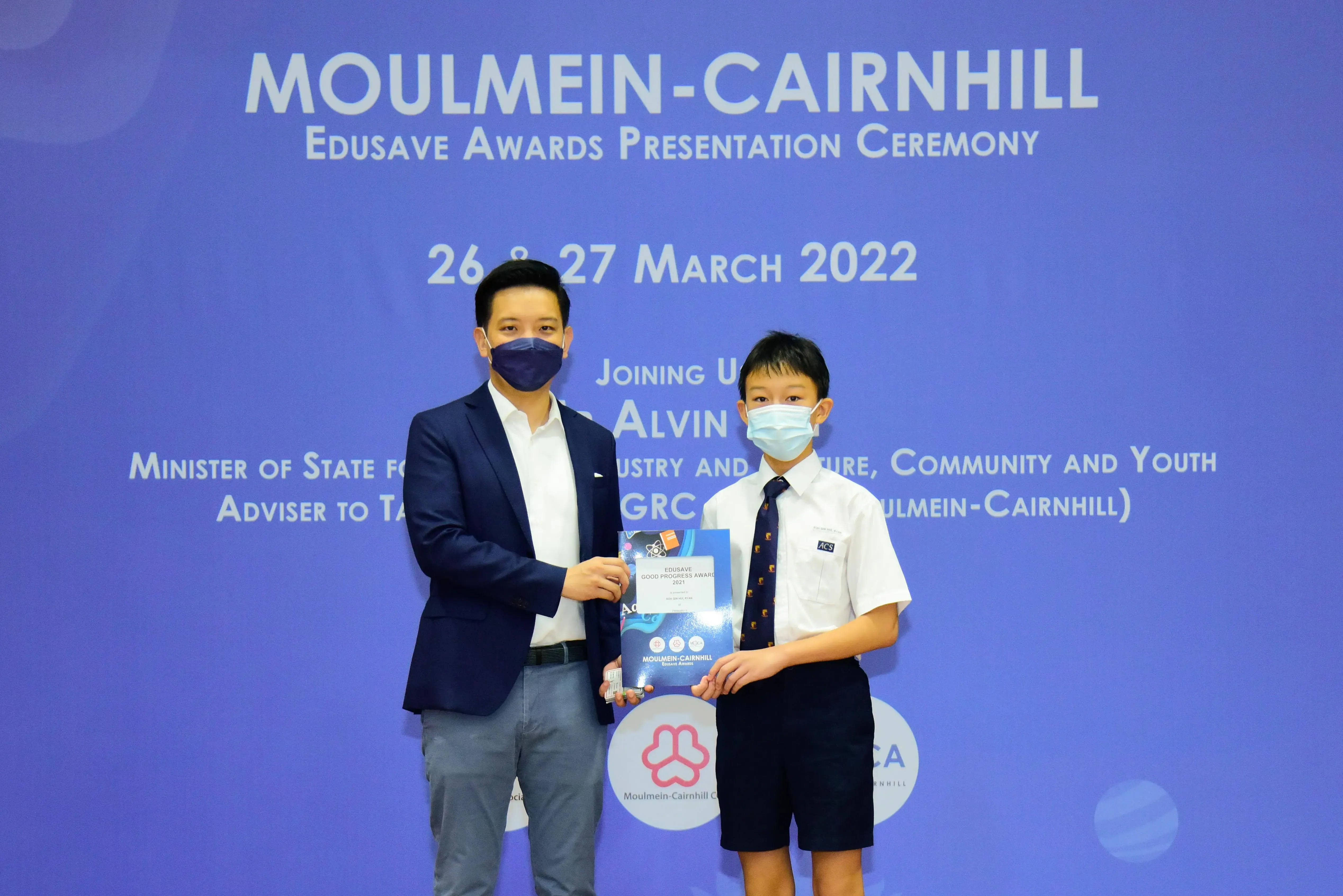 An adult and a young student in school uniform hold an award certificate at the Moulmein-Cairnhill Edusave Awards Ceremony.