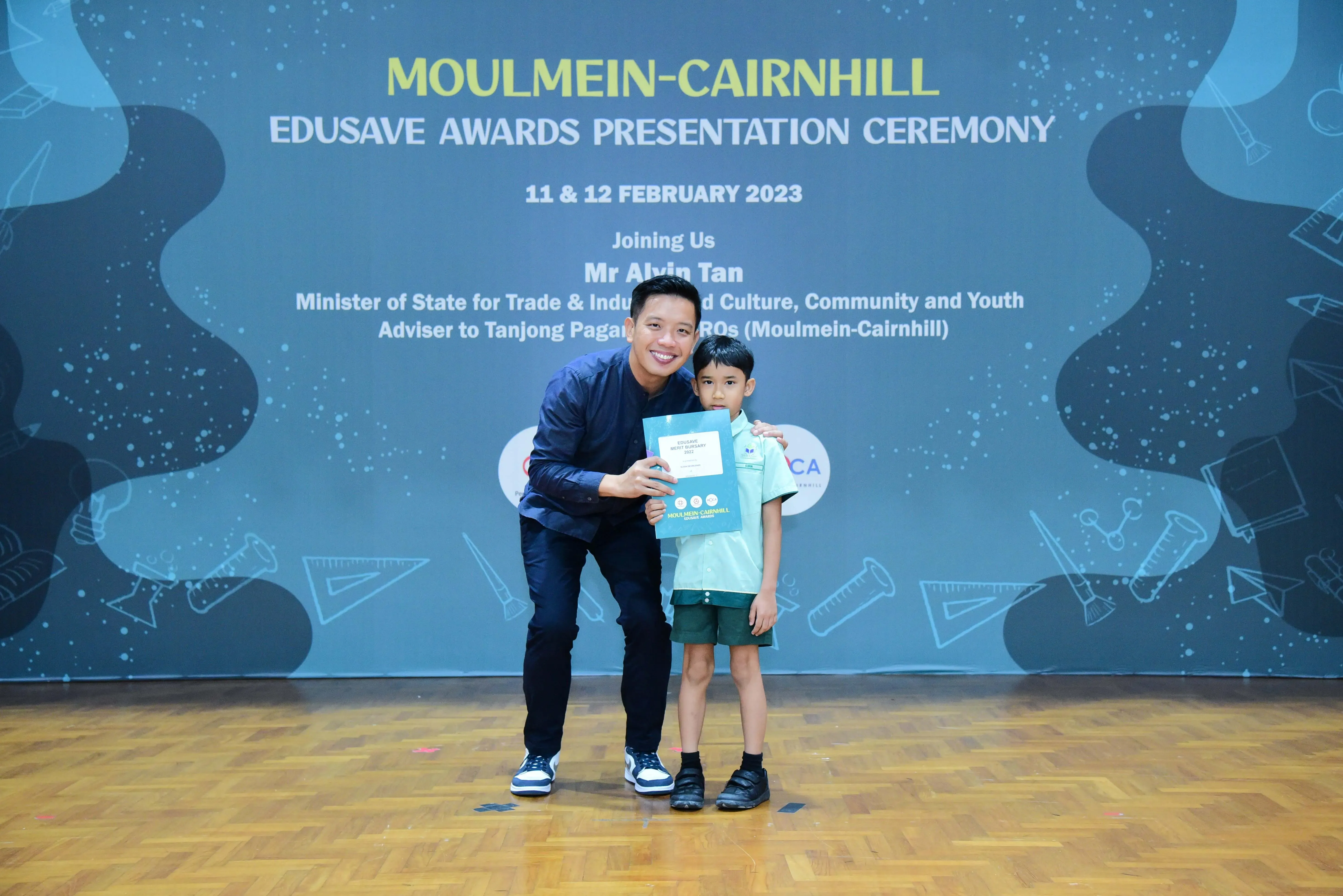 A man and a young boy hold a certificate at the Moulmein-Cairnhill Edusave Awards Presentation Ceremony, February 2023.