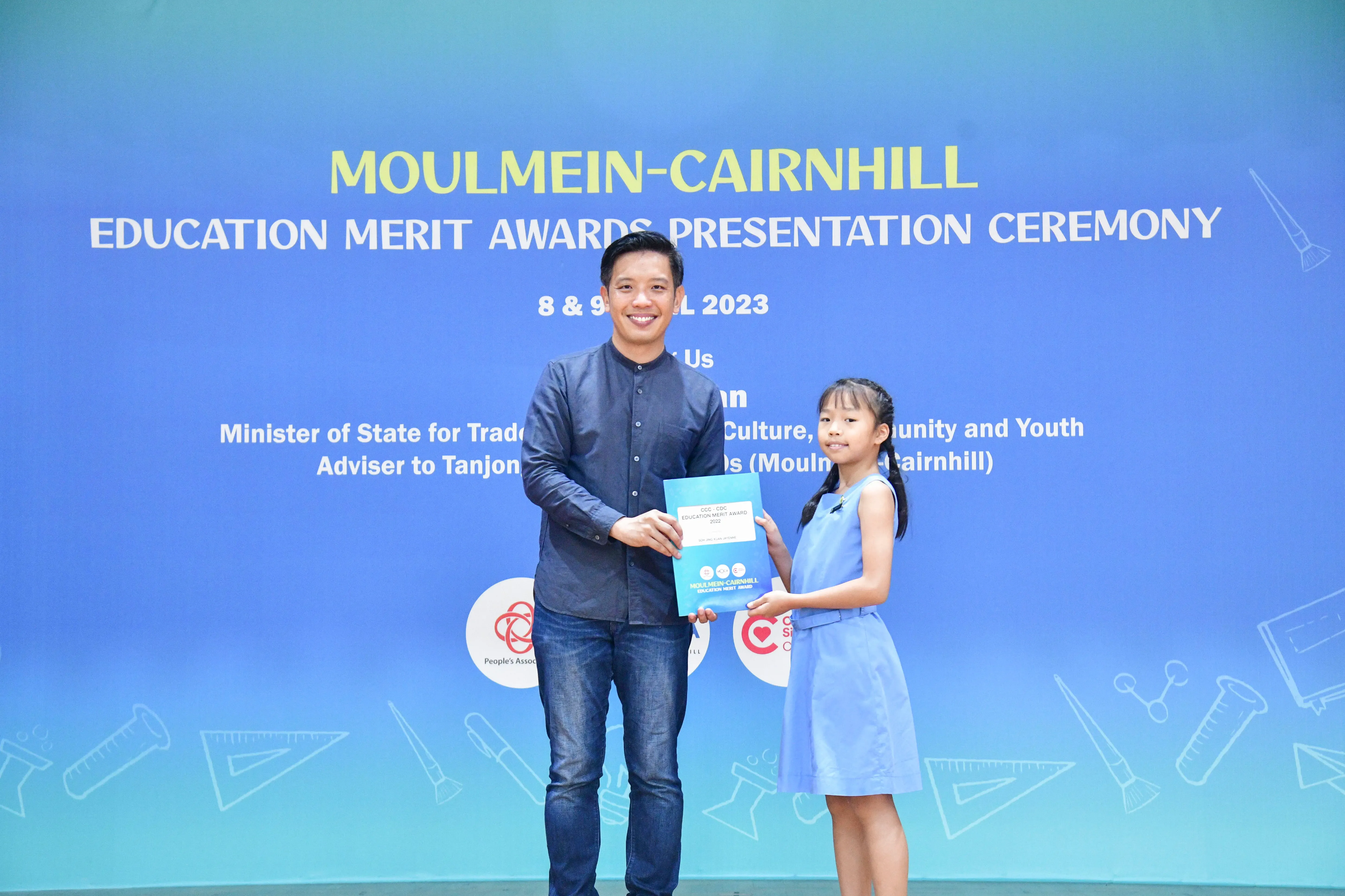 A man and a young girl hold a certificate together at the Moulmein-Cairnhill Education Merit Awards Ceremony 2023.