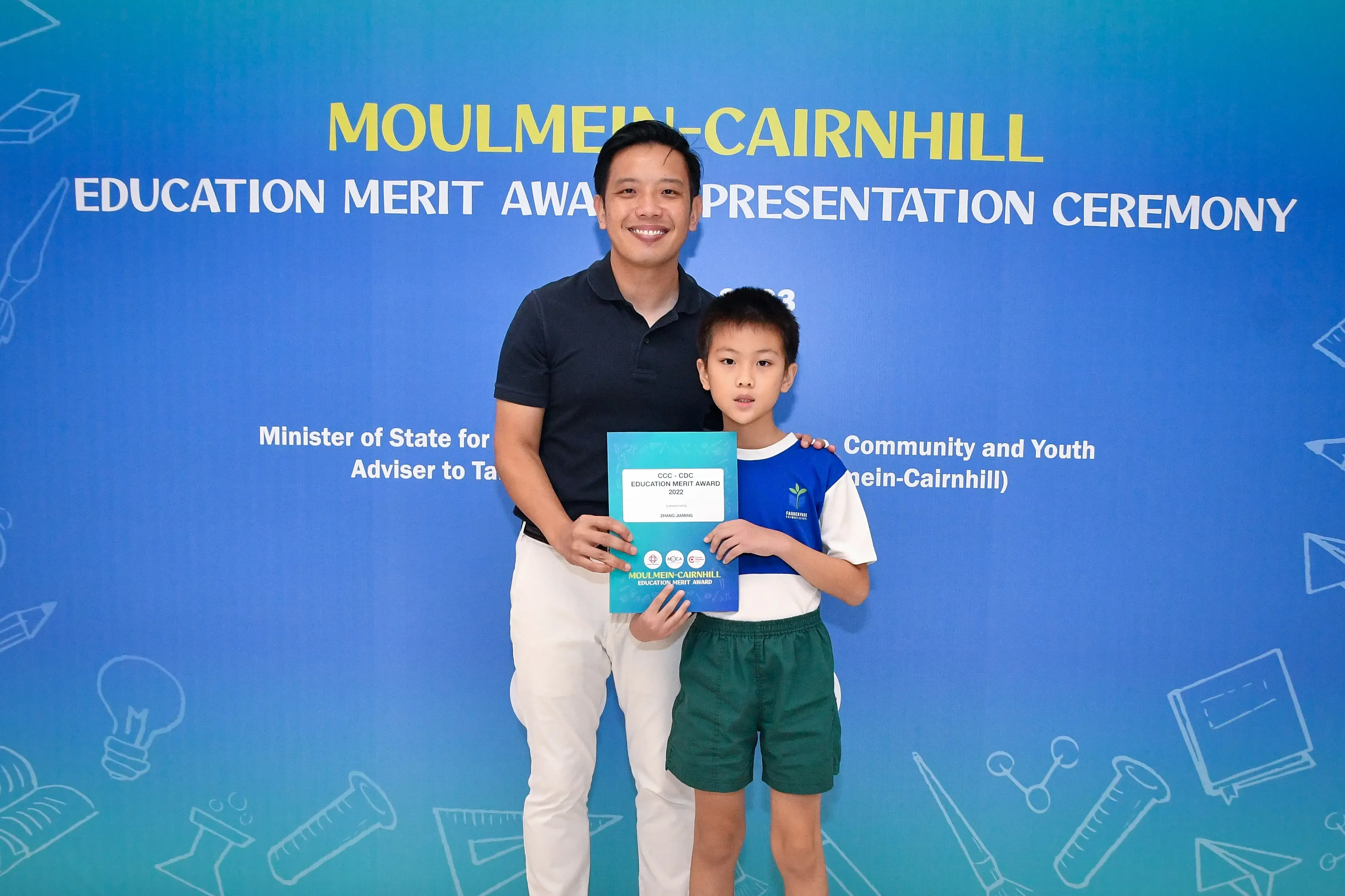 A man and a young boy pose together holding an award certificate at the Moulmein-Cairnhill Education Merit Award ceremony.