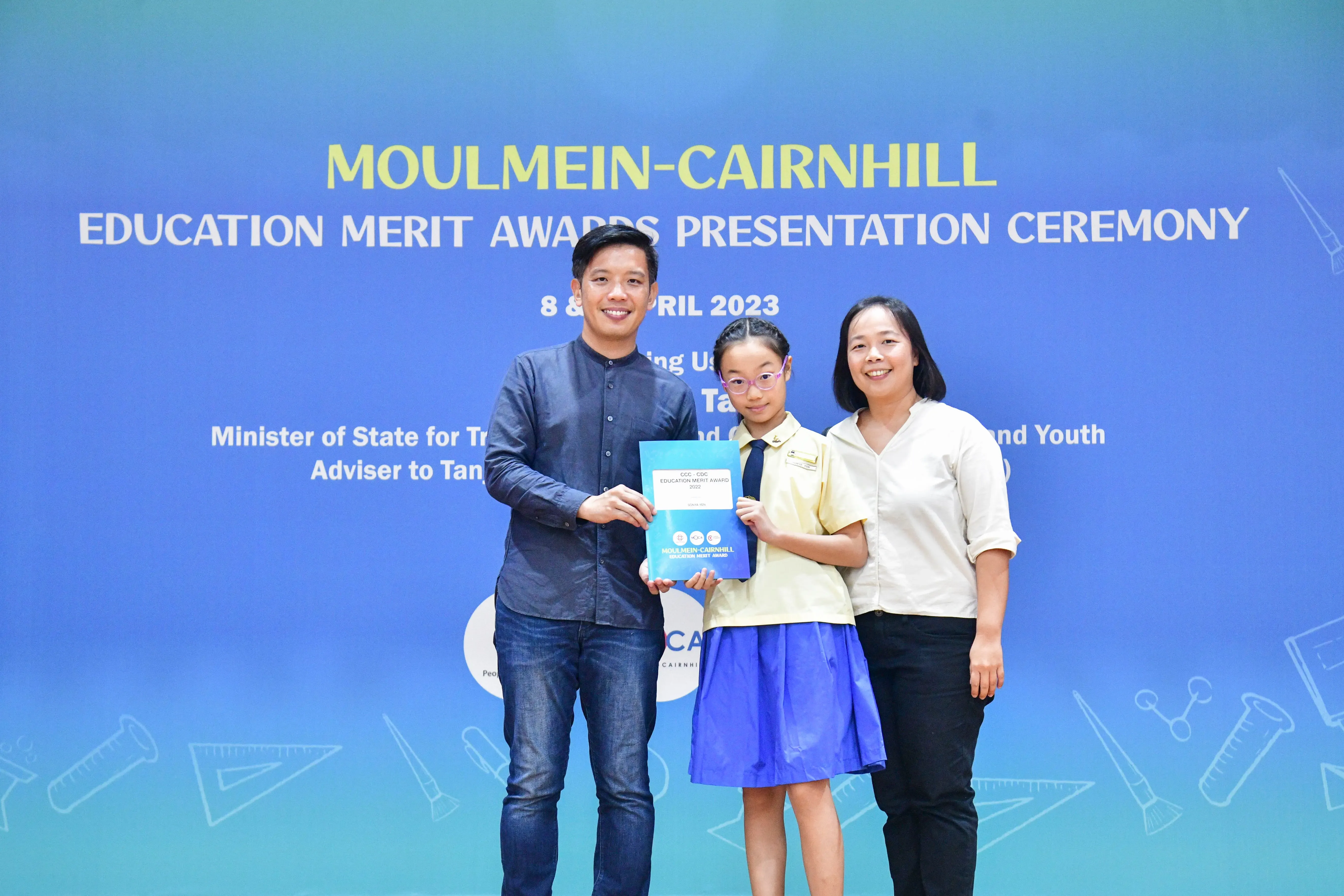 A man and woman stand with a young girl holding an award at the Moulmein-Cairnhill Education Merit Awards 2023.