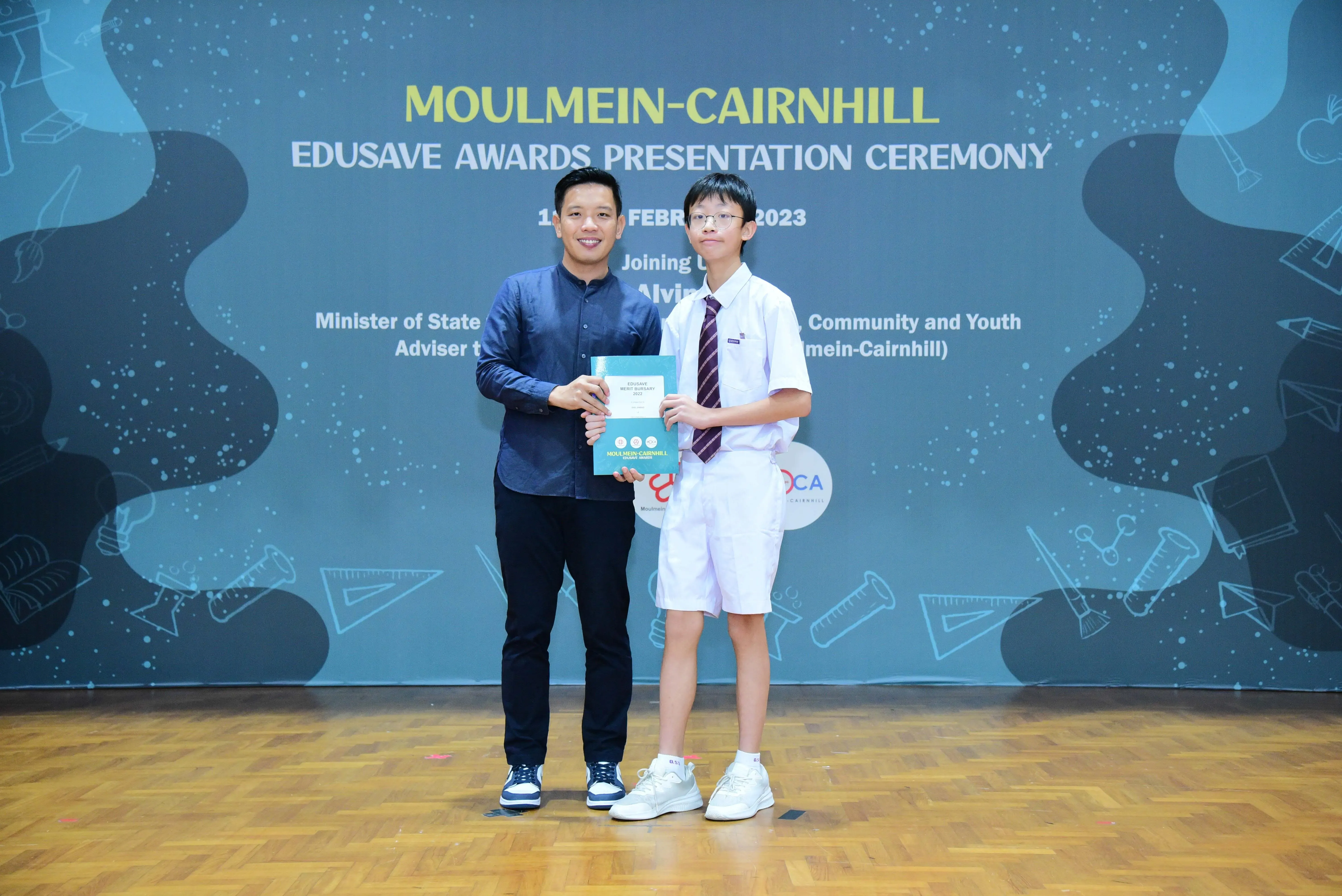 An adult and a uniformed student hold an award together at the Moulmein-Cairnhill Edusave Awards Ceremony 2023.
