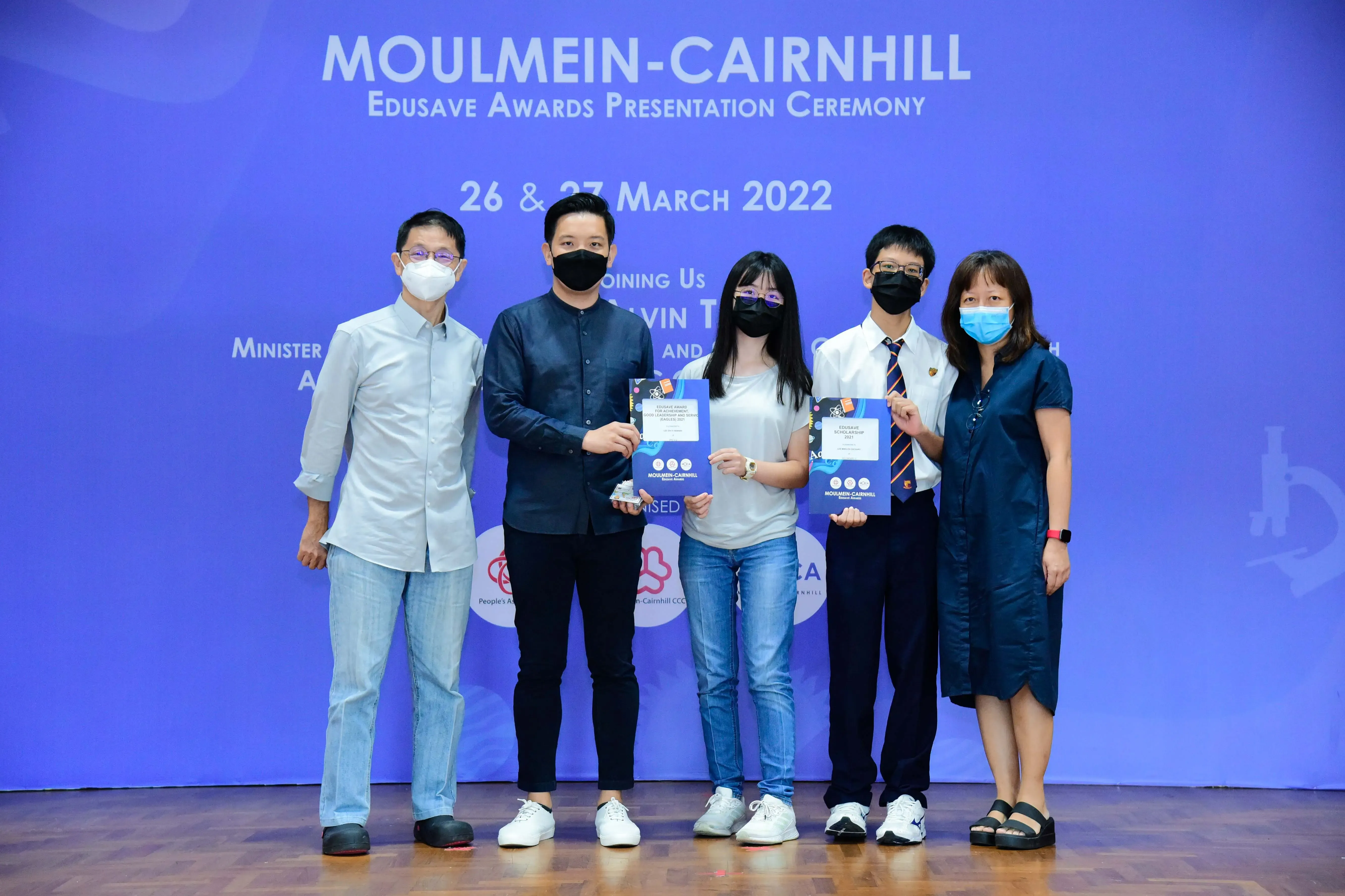 Five masked people pose on stage at the Moulmein-Cairnhill Edusave Awards Presentation Ceremony, March 2022.