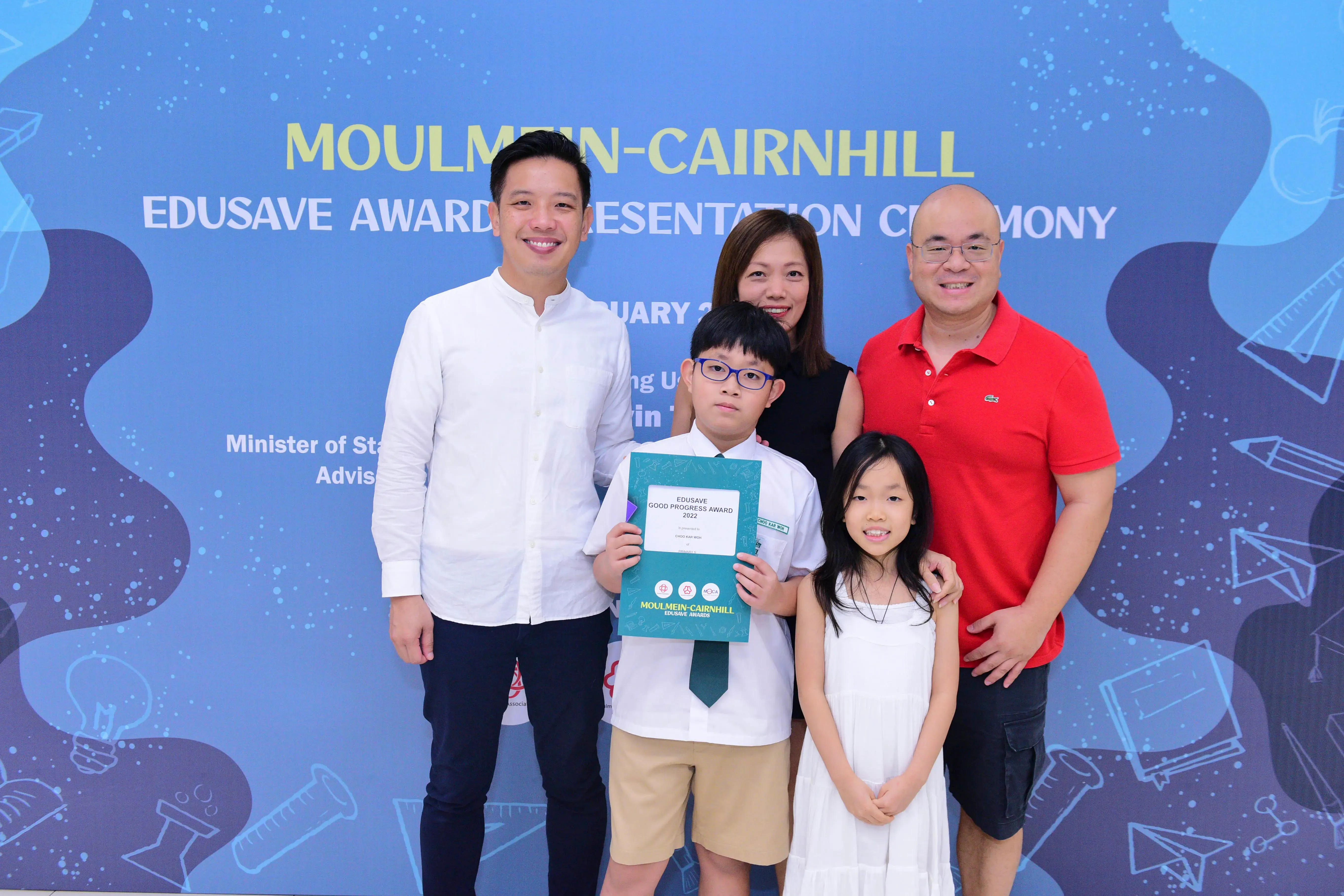 Five people pose at the Moulmein-Cairnhill Edusave Award Presentation Ceremony; a boy holds a certificate.