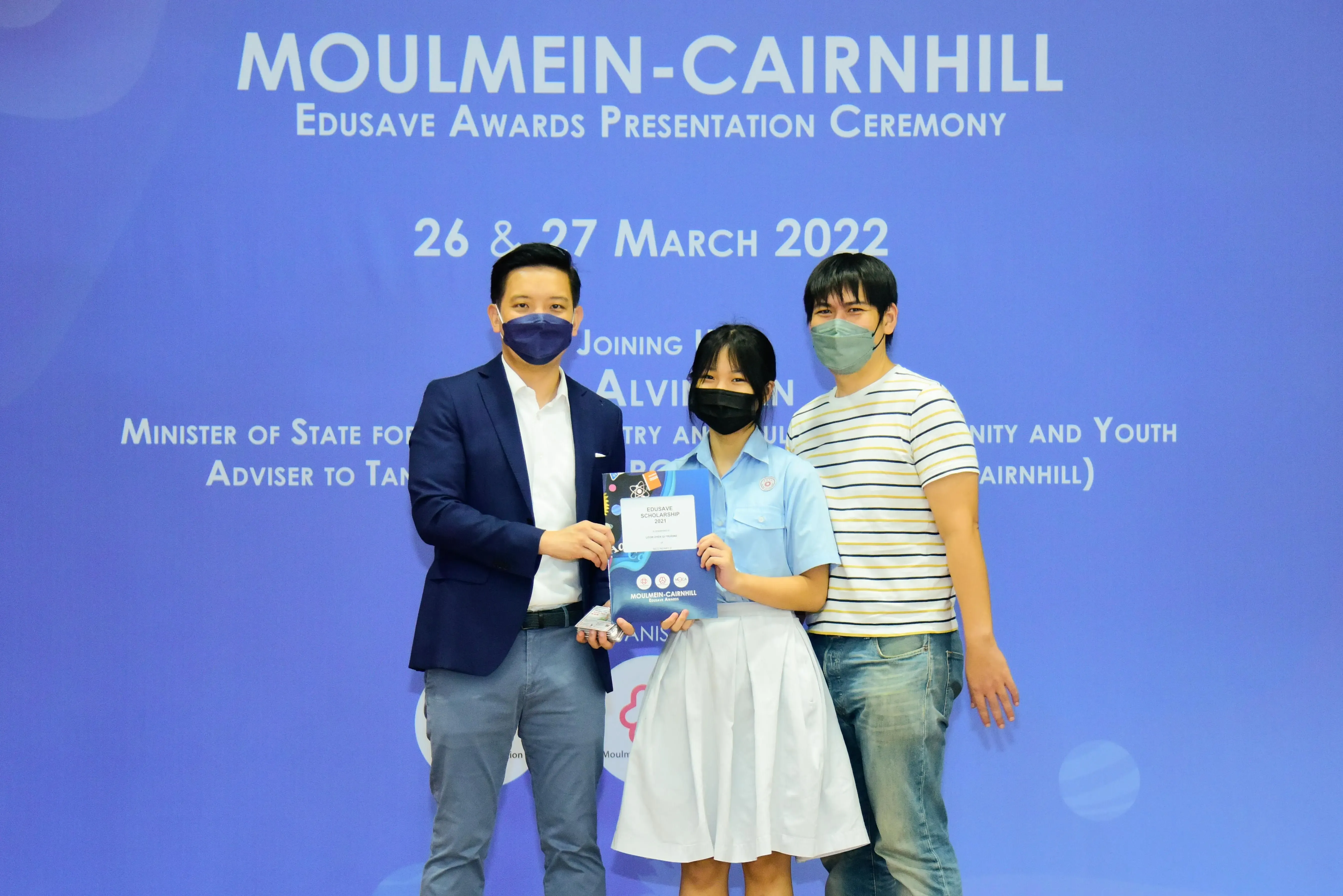 Three masked people pose holding an award folder at the Moulmein-Cairnhill Edusave Awards Ceremony, March 2022.