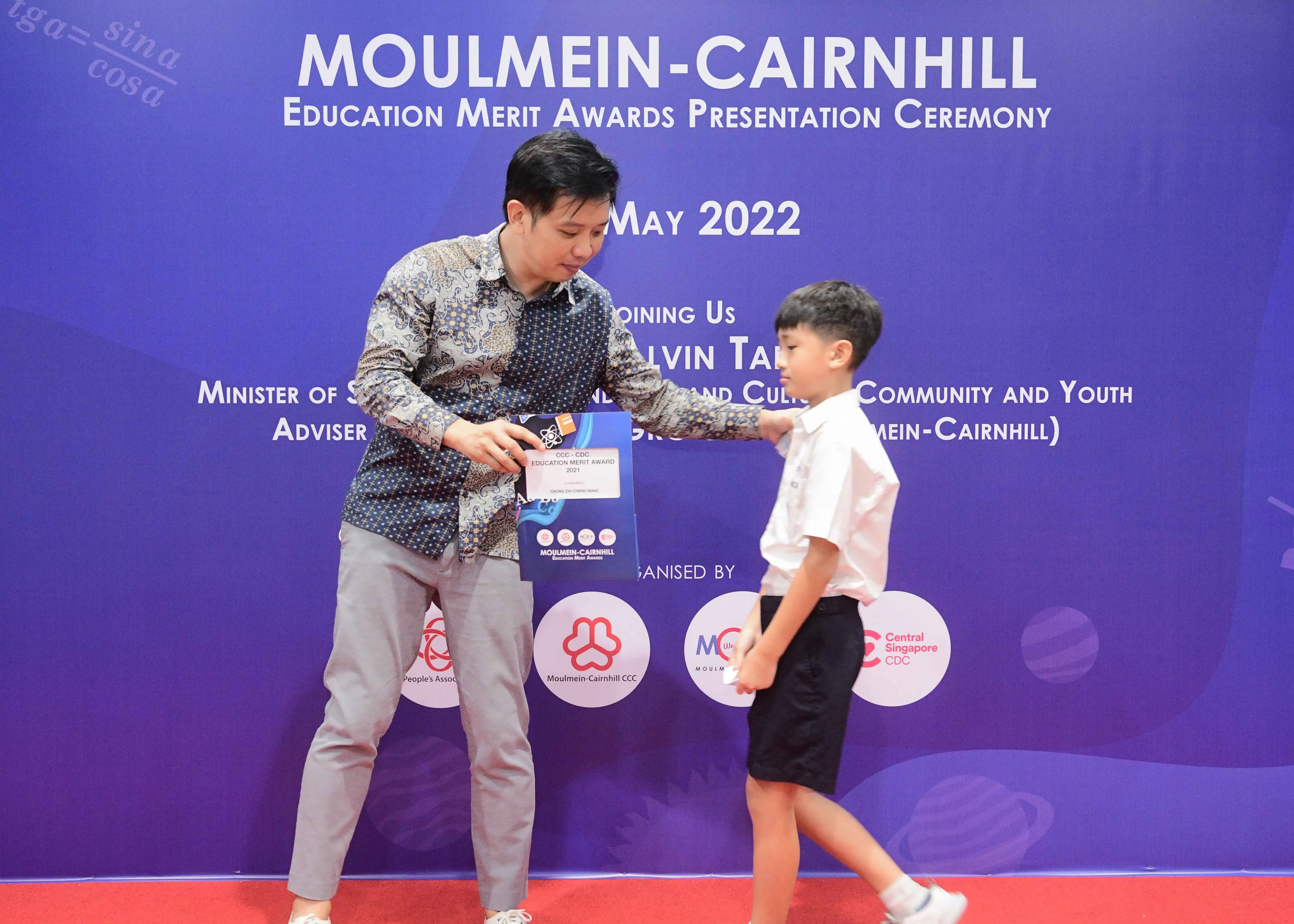 A man hands an award to a young boy at the Moulmein-Cairnhill Education Merit Awards Ceremony, May 2022.