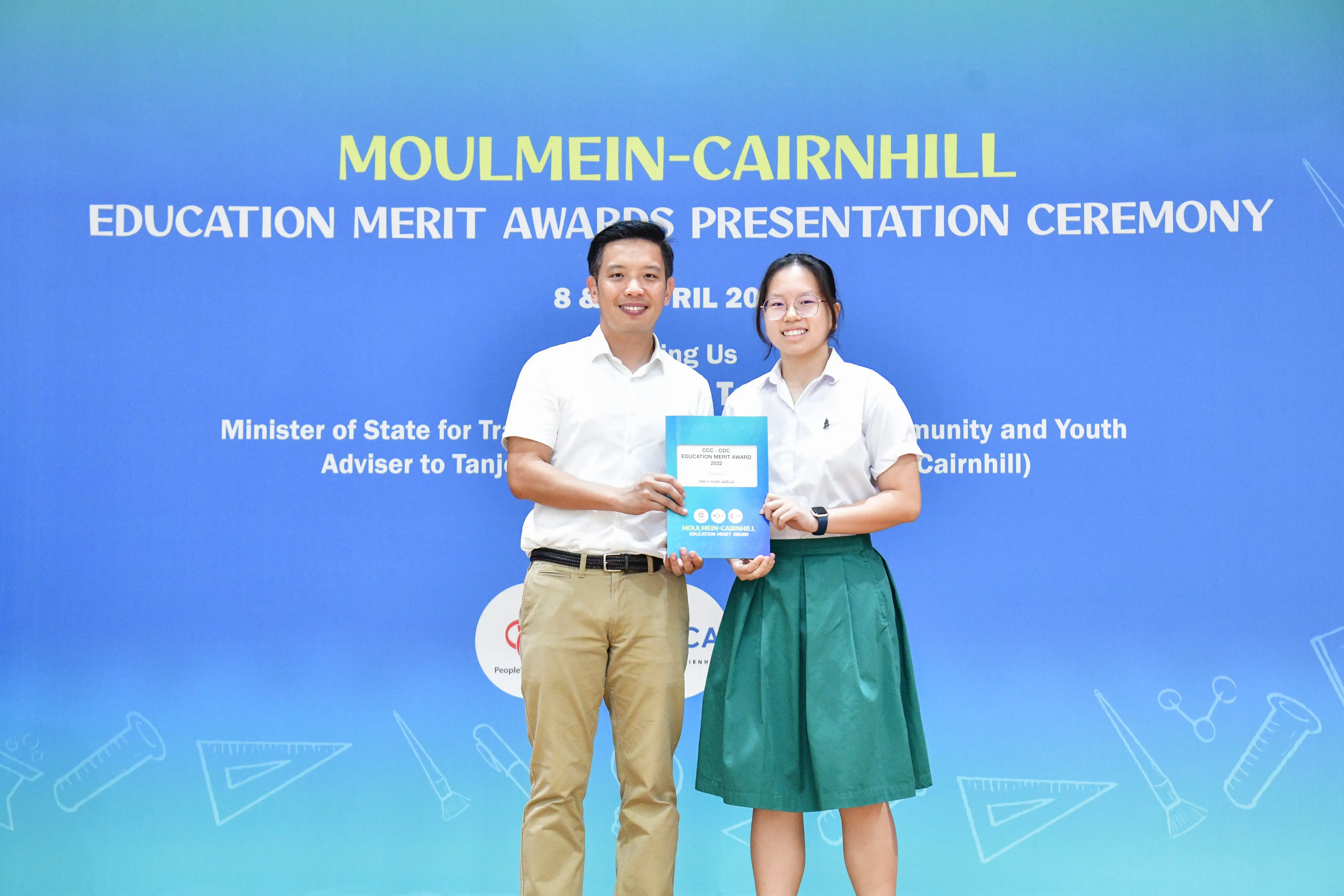 Two people smile while holding an award booklet at the Moulmein-Cairnhill Education Merit Awards Presentation Ceremony.