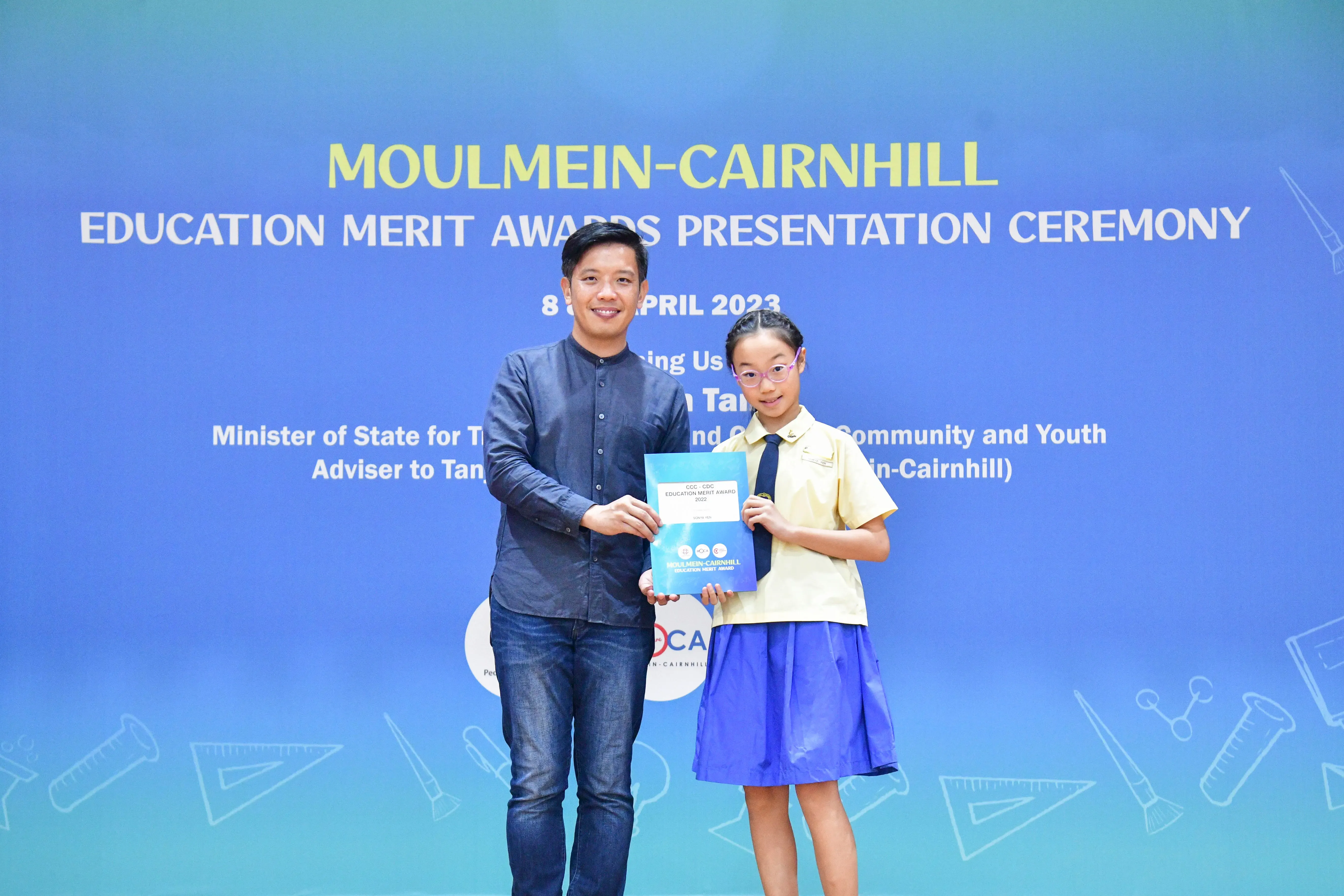 A man and a young girl hold an award certificate at the Moulmein-Cairnhill Education Merit Awards Ceremony 2023.
