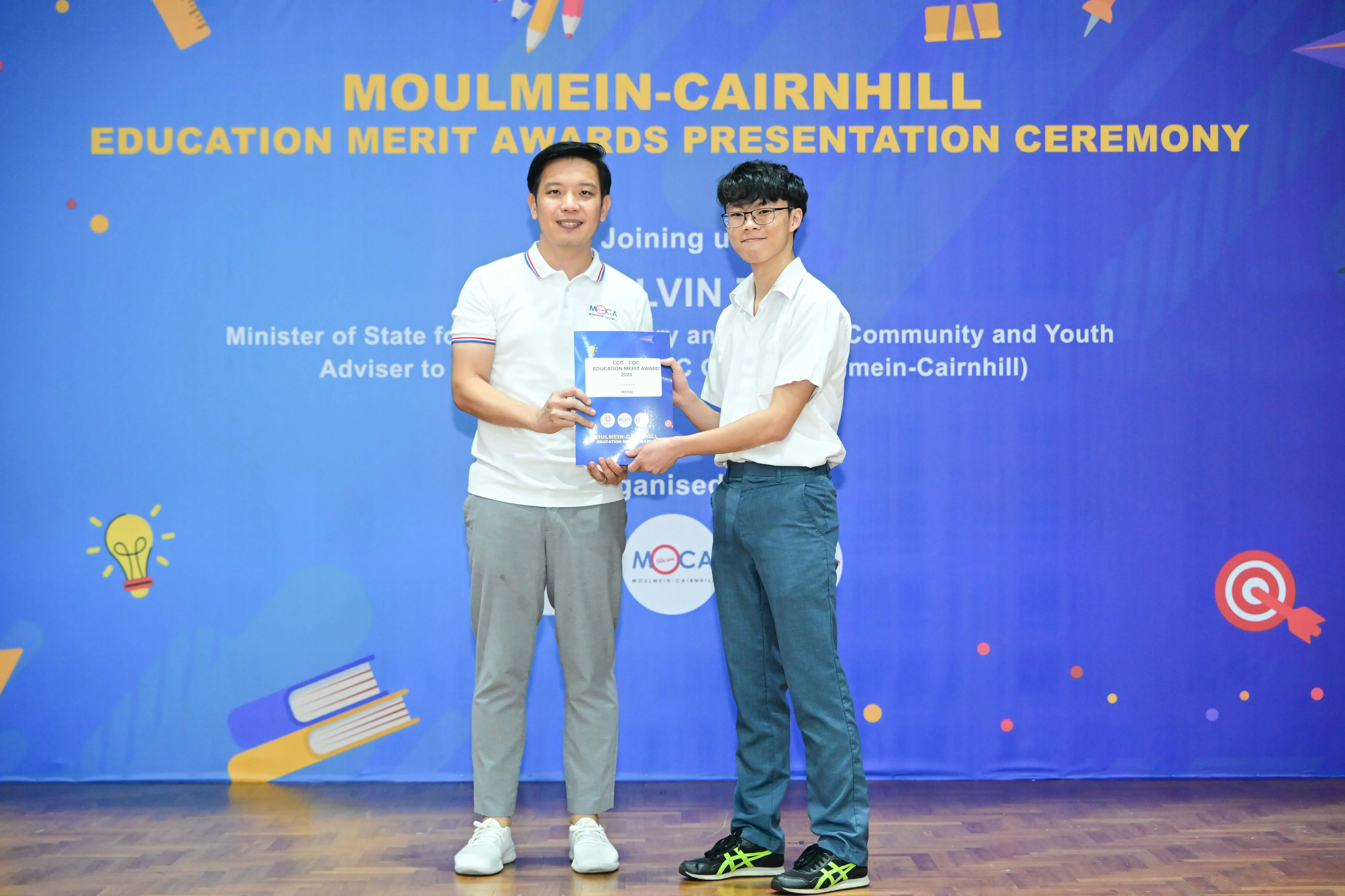 Two men hold a certificate together at the Moulmein-Cairnhill Education Merit Awards Presentation Ceremony.
