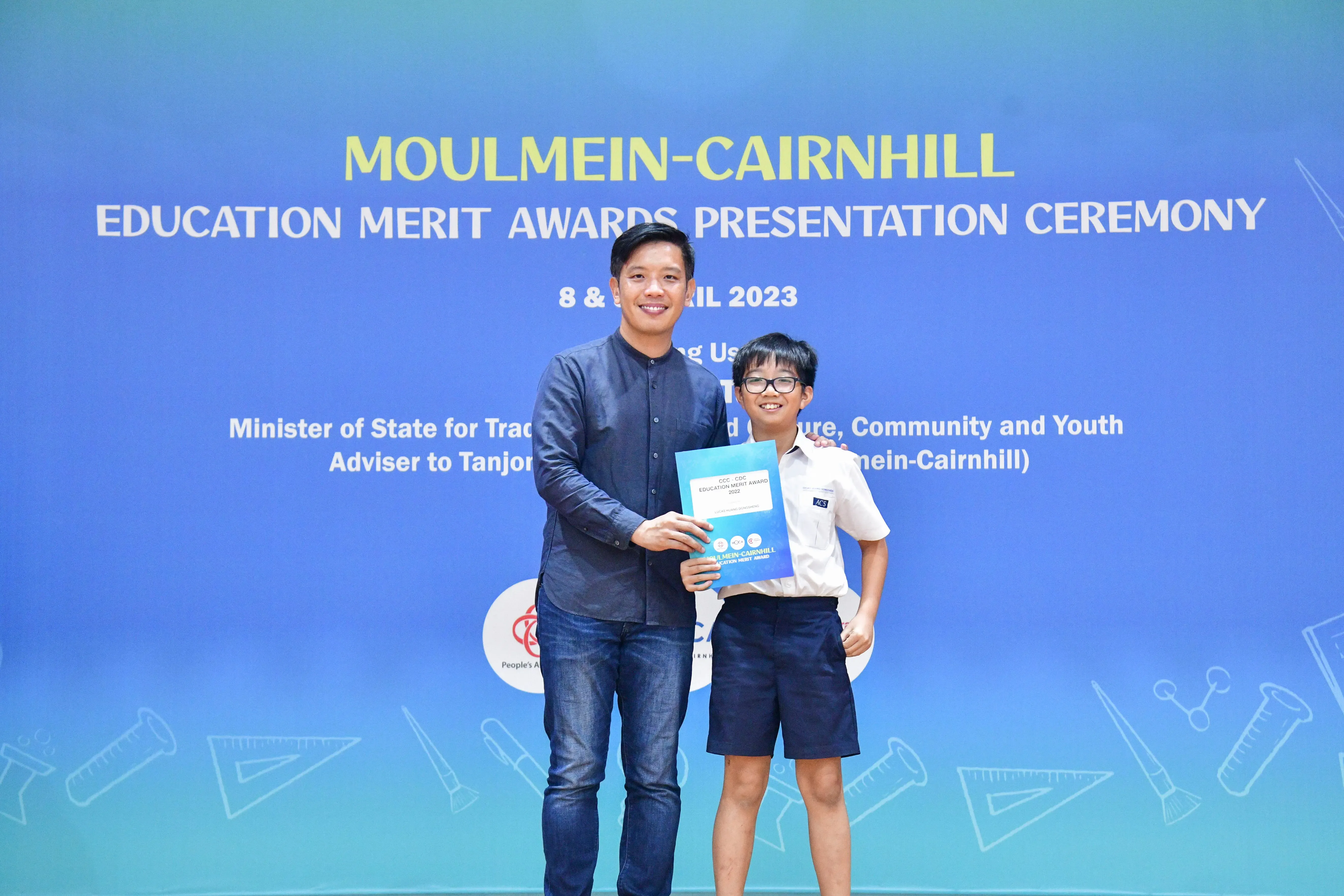 An adult and a young boy hold an award certificate at the Moulmein-Cairnhill Education Merit Awards Ceremony 2023.