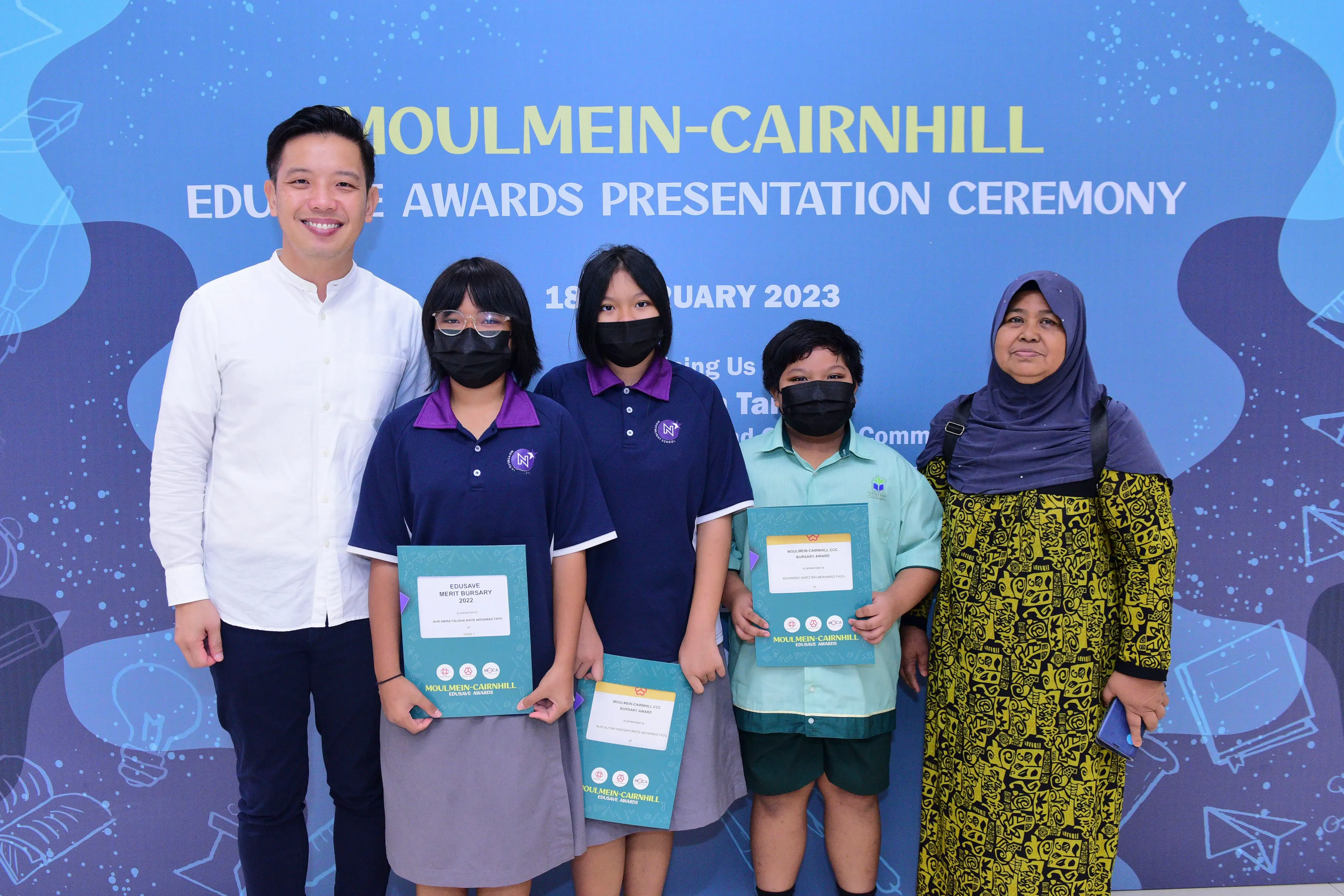 Three masked children holding award certificates pose with two adults at the Moulmein-Cairnhill Edusave Awards Ceremony 2023.
