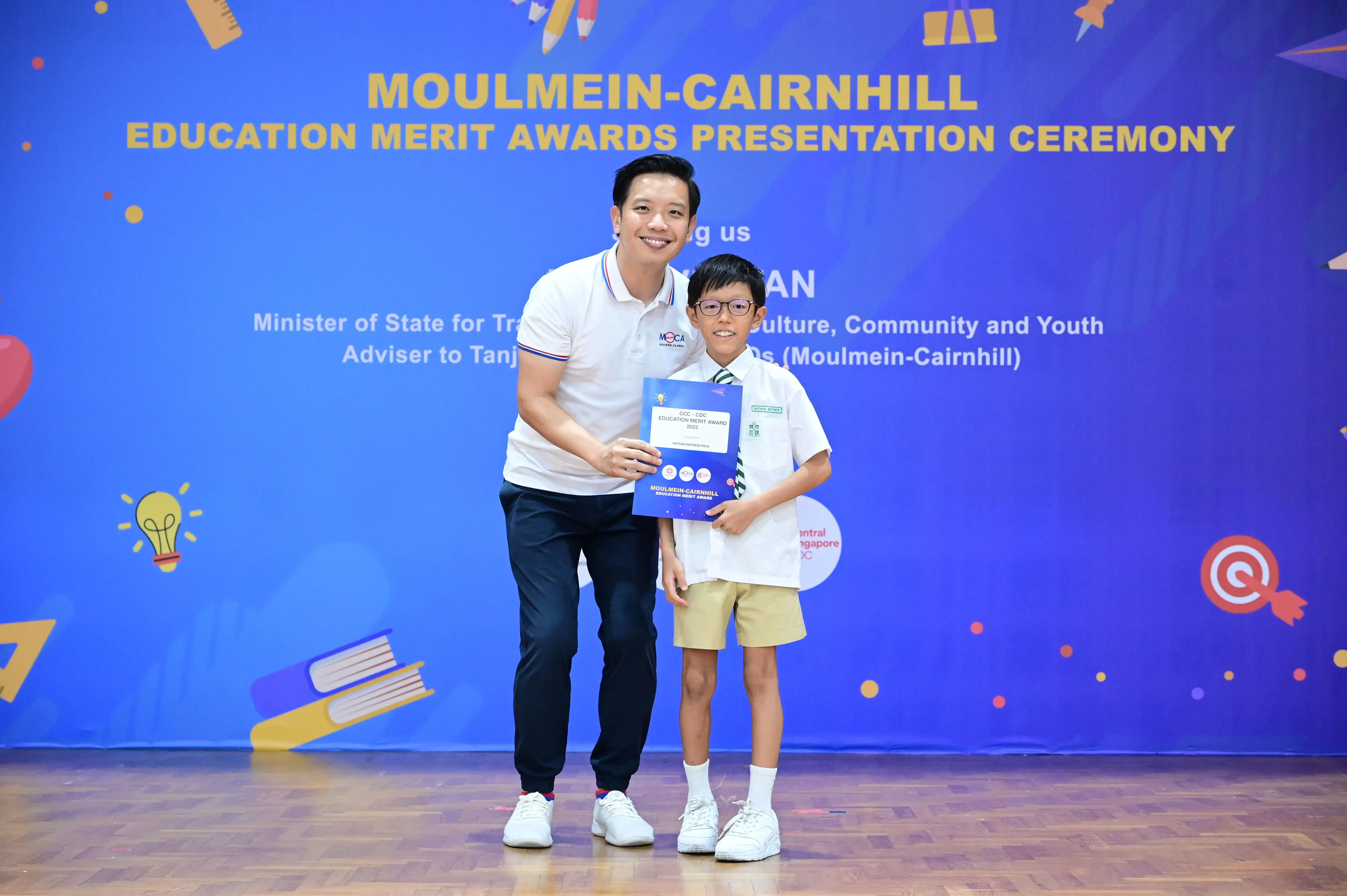 Adult and young boy holding a certificate at Moulmein-Cairnhill Education Merit Awards Presentation Ceremony.