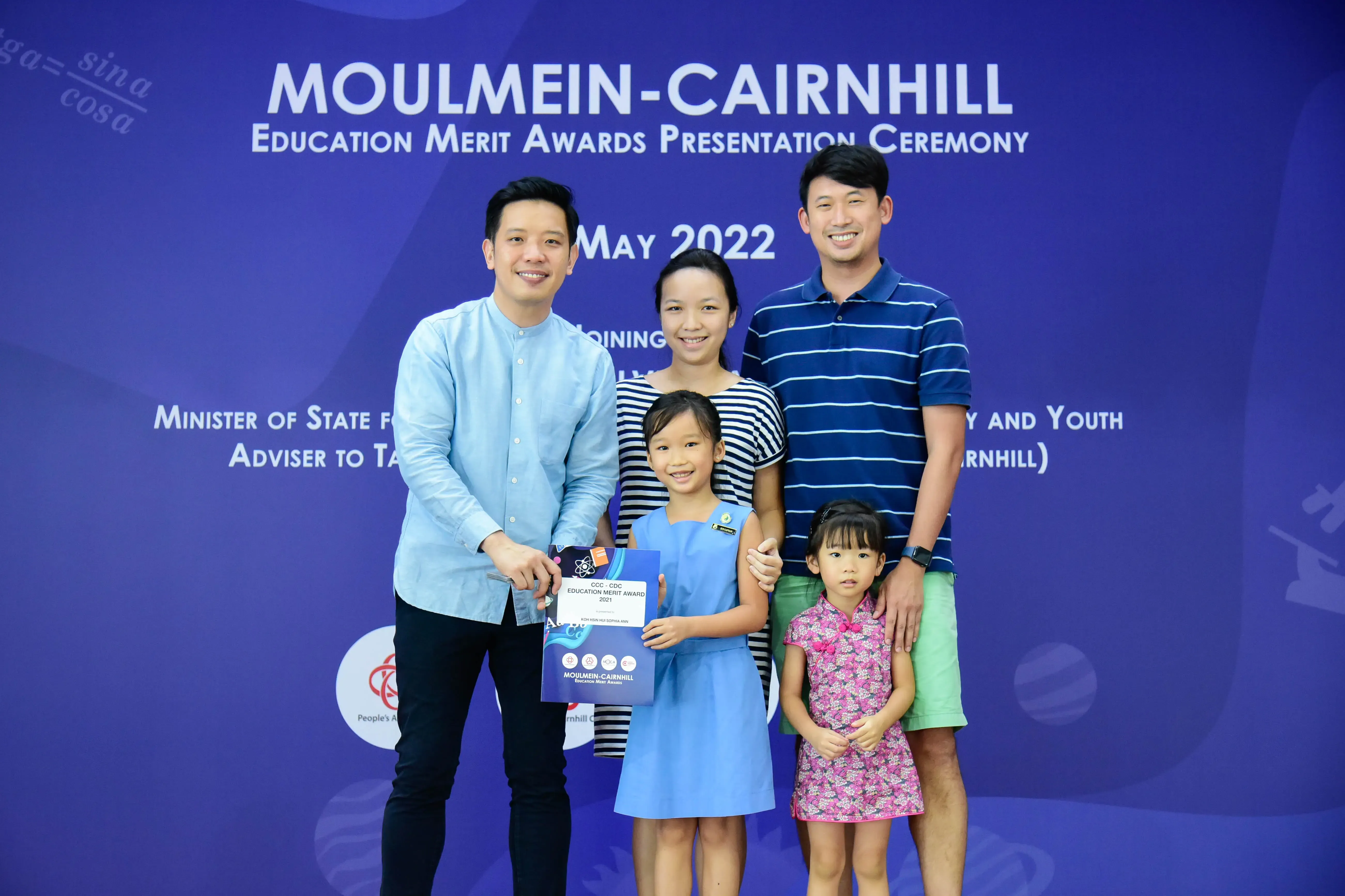 Five people pose at the Moulmein-Cairnhill Education Merit Awards Presentation Ceremony, May 2022, with a girl holding an award.