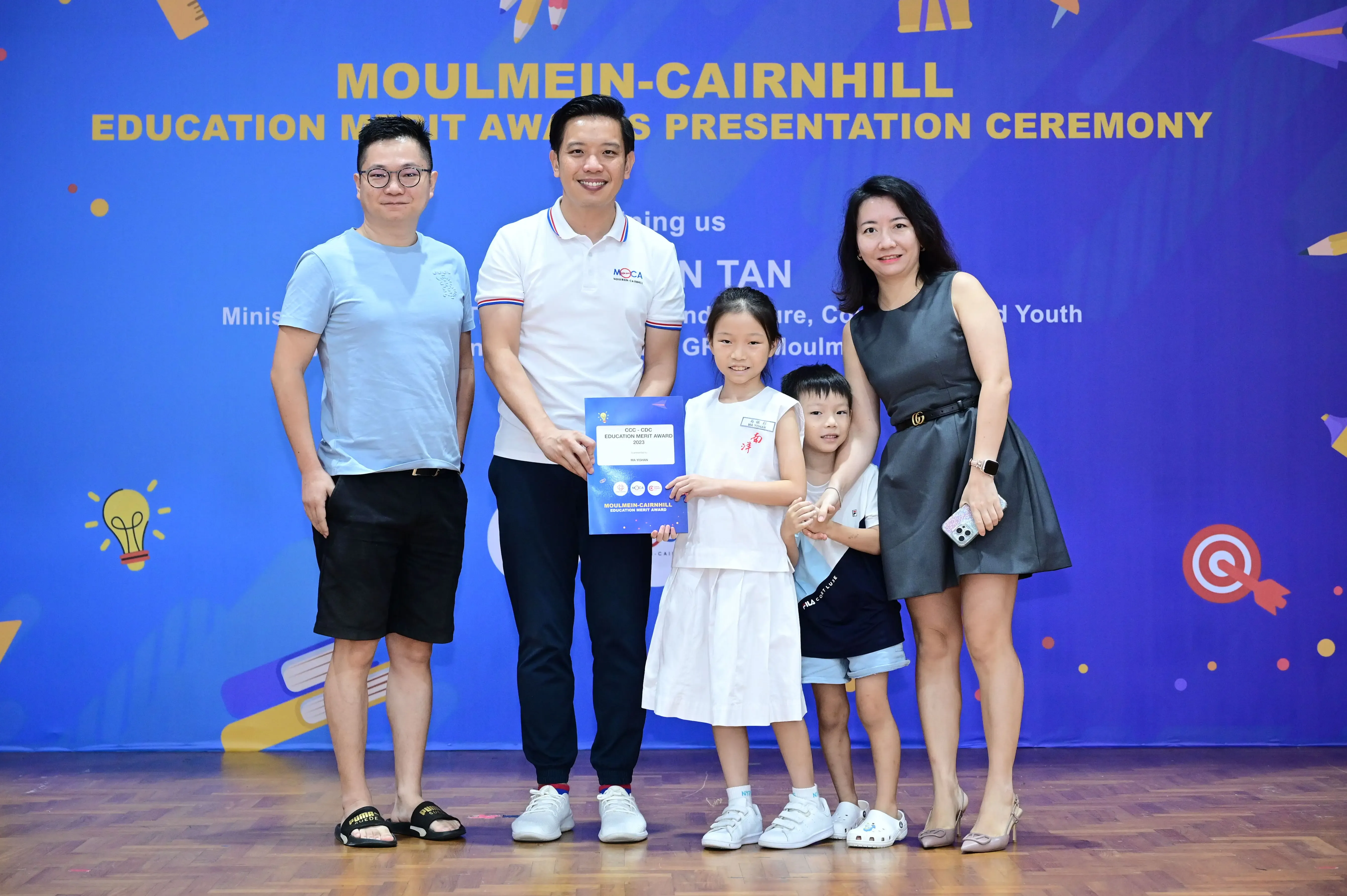 Two adults and two children pose with a certificate at the Moulmein-Cairnhill Education Merit Awards Presentation Ceremony.