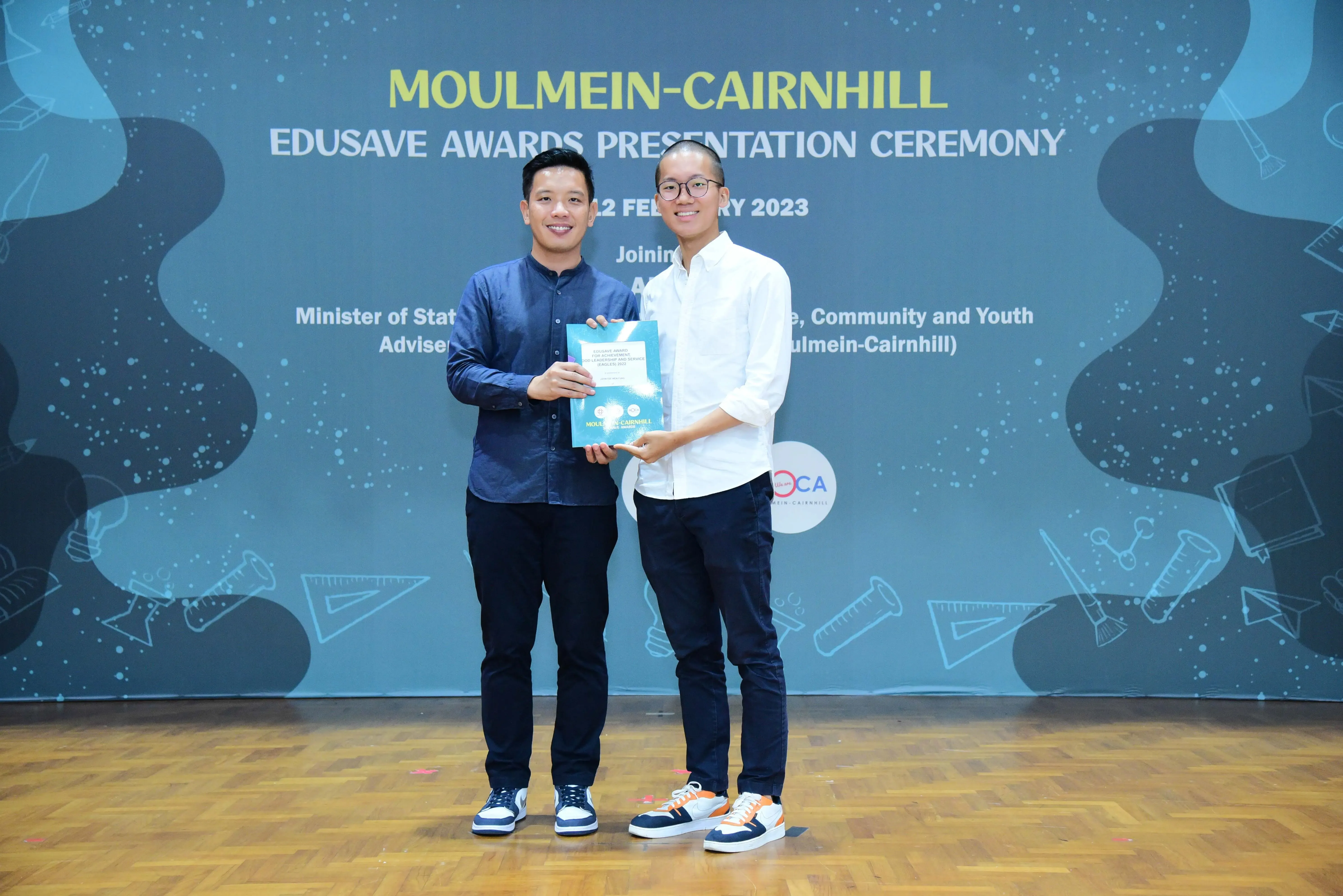 Two men smiling and holding a certificate at the Moulmein-Cairnhill Edusave Awards Presentation Ceremony 2023.