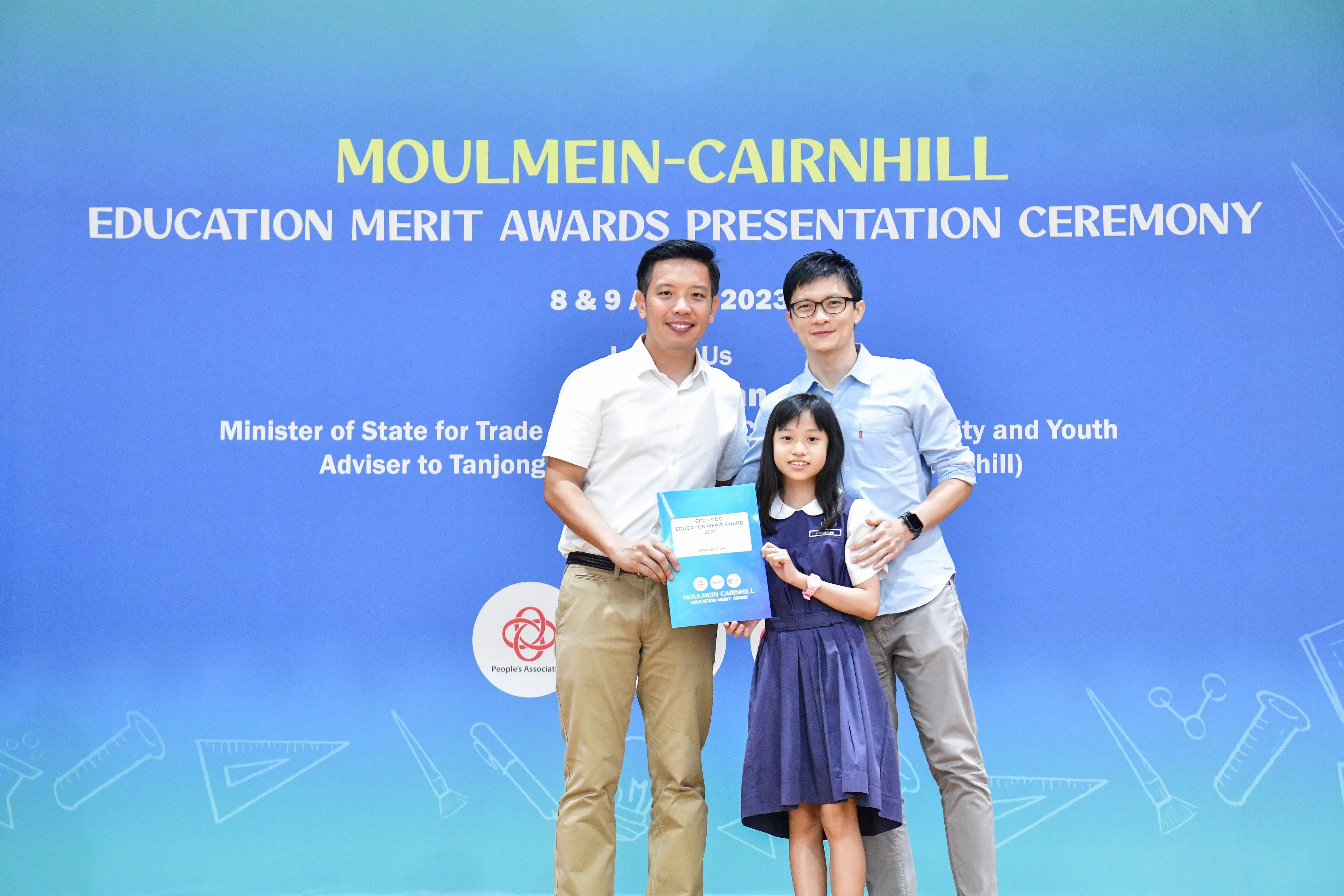 Two men and a young girl pose holding a certificate at the Moulmein-Cairnhill Education Merit Awards Ceremony 2023.