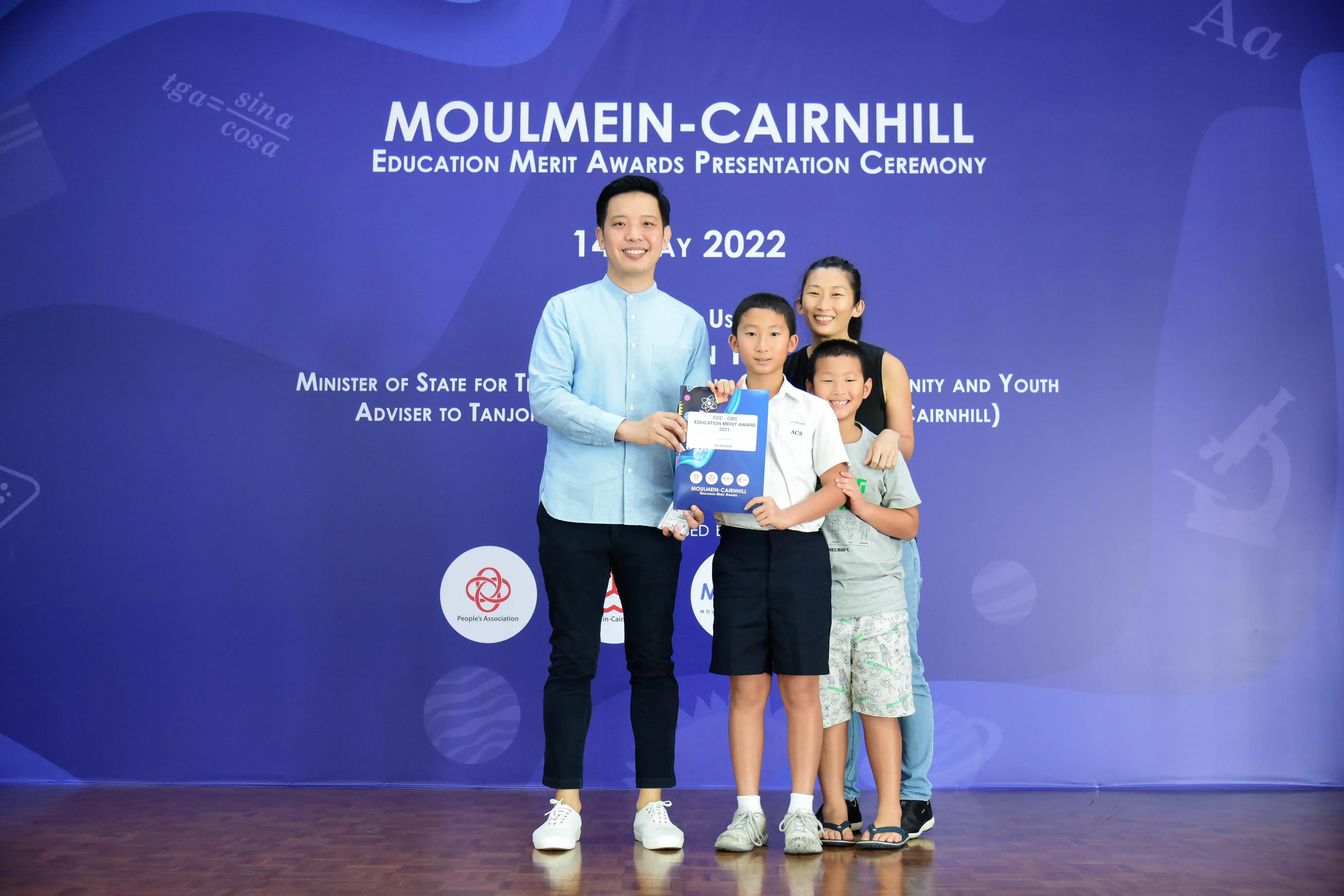 A man and a woman pose with two young boys holding an award certificate at the Moulmein-Cairnhill Education Merit Awards 2022.